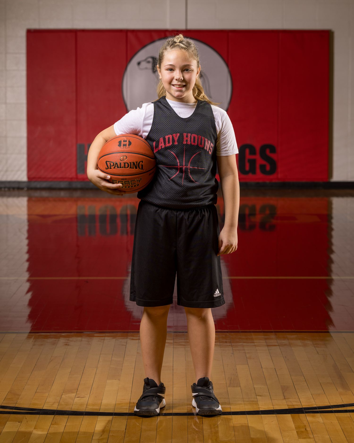 Young basketball player in Lady Houns uniform holds basketball in gymnasium.