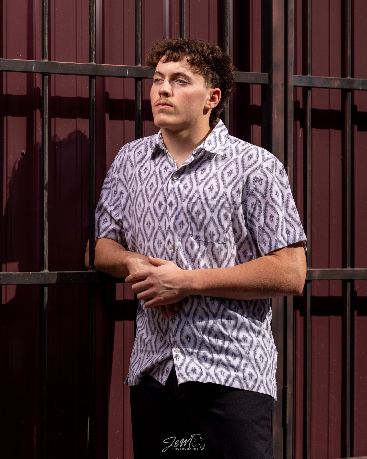 Portrait against red metal backdrop wearing patterned short sleeve button-up shirt.