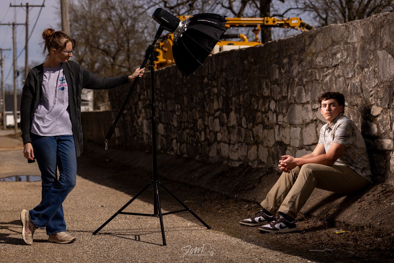 A photography setup with lighting and camera equipment against a stone wall during golden hour.