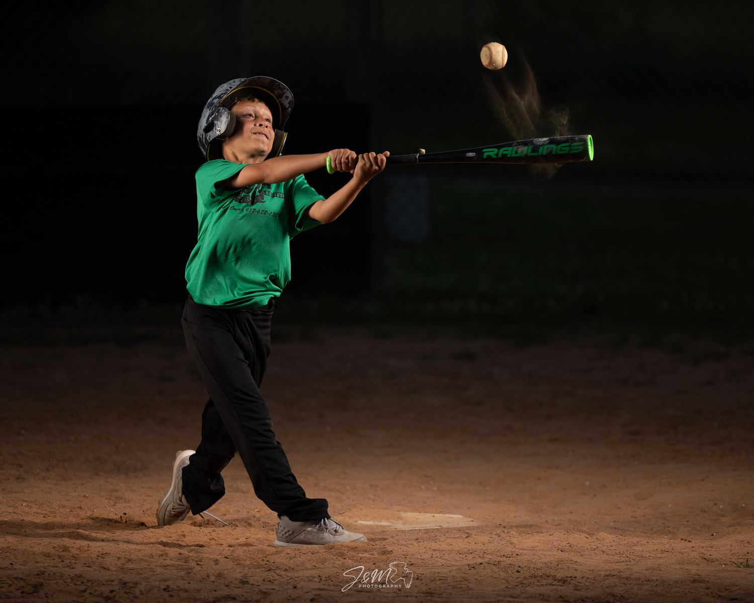 Baseball batter in green jersey following through on swing during nighttime game.