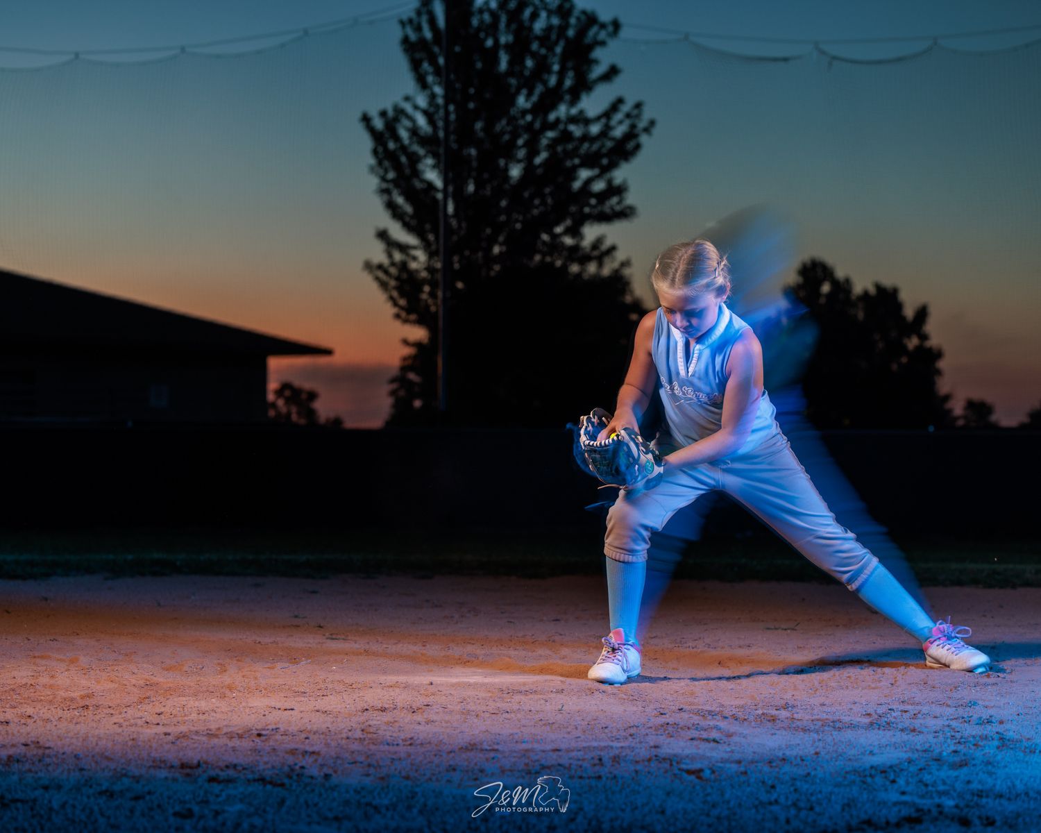 Baseball player in action stance captured at sunset with blue lighting effects.