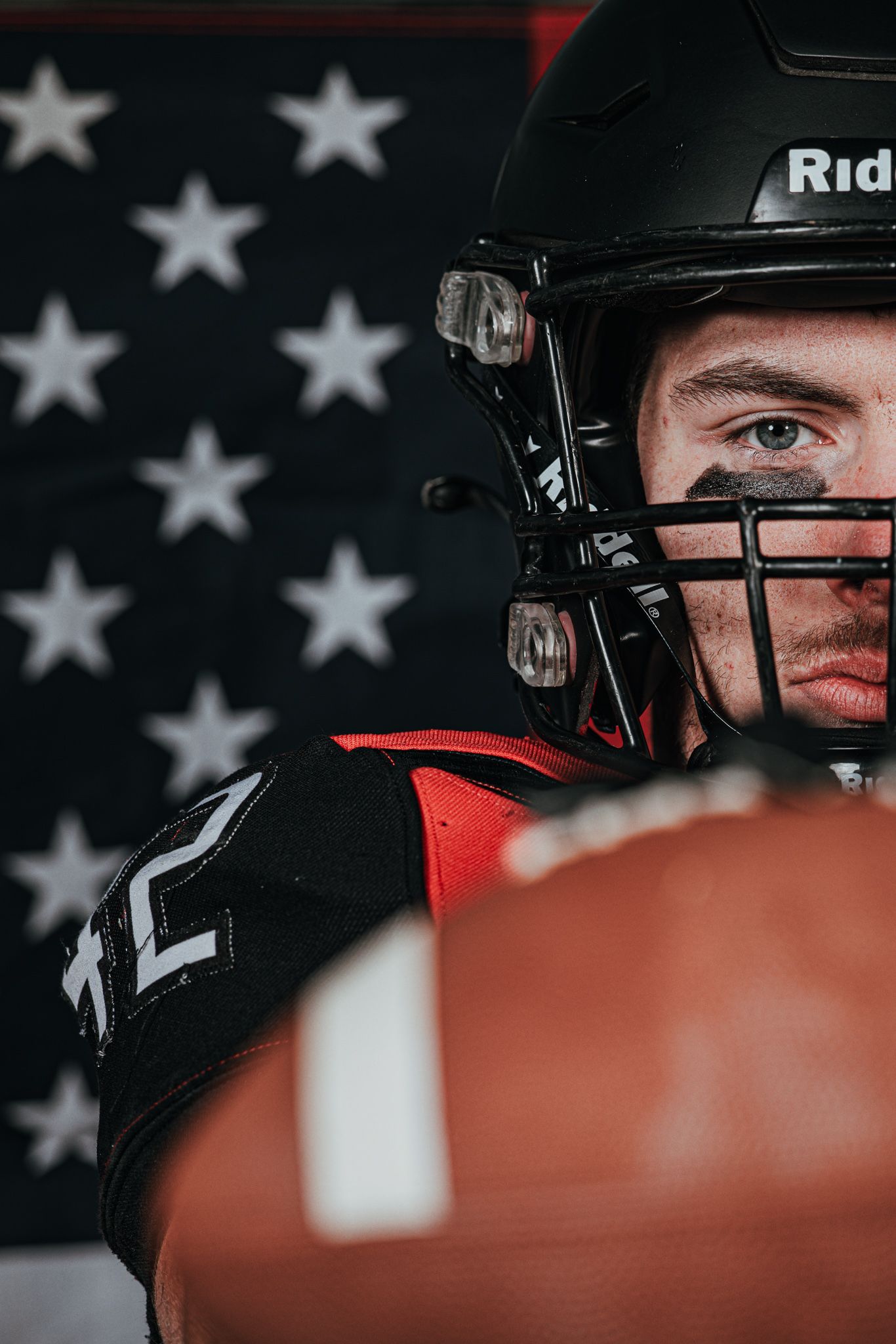 Close-up football portrait with American flag backdrop and protective helmet.