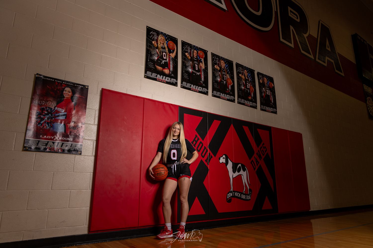 Athletic portrait in a gymnasium with red walls and team photos displayed.