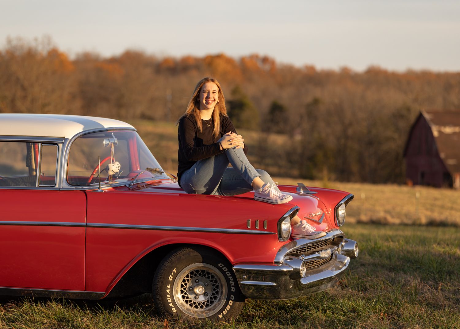 Person sitting on vintage red Chevrolet car in autumn field setting.