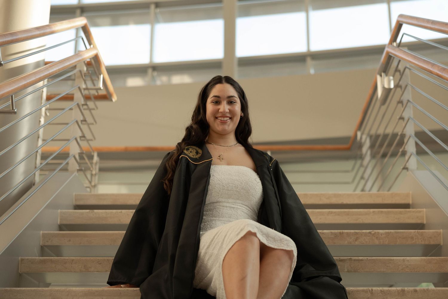 Kennesaw State University Graduate in academic regalia seated on modern indoor staircase.
