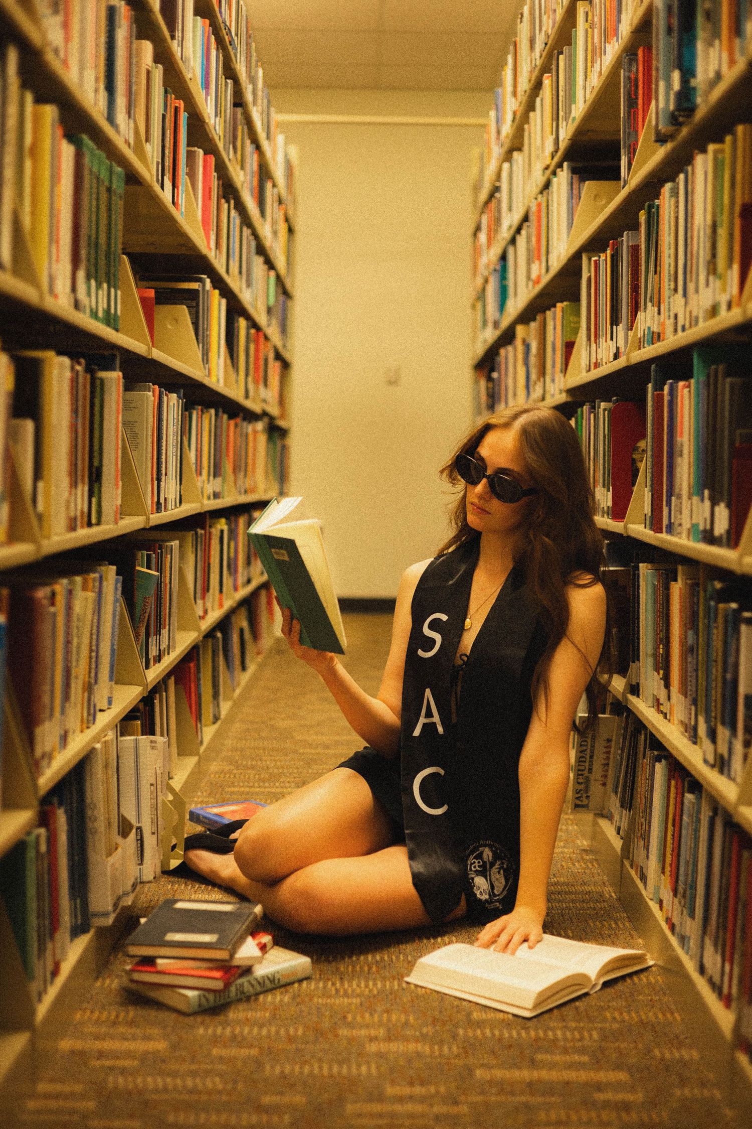 Student studying with books while sitting on library floor wearing sunglasses.