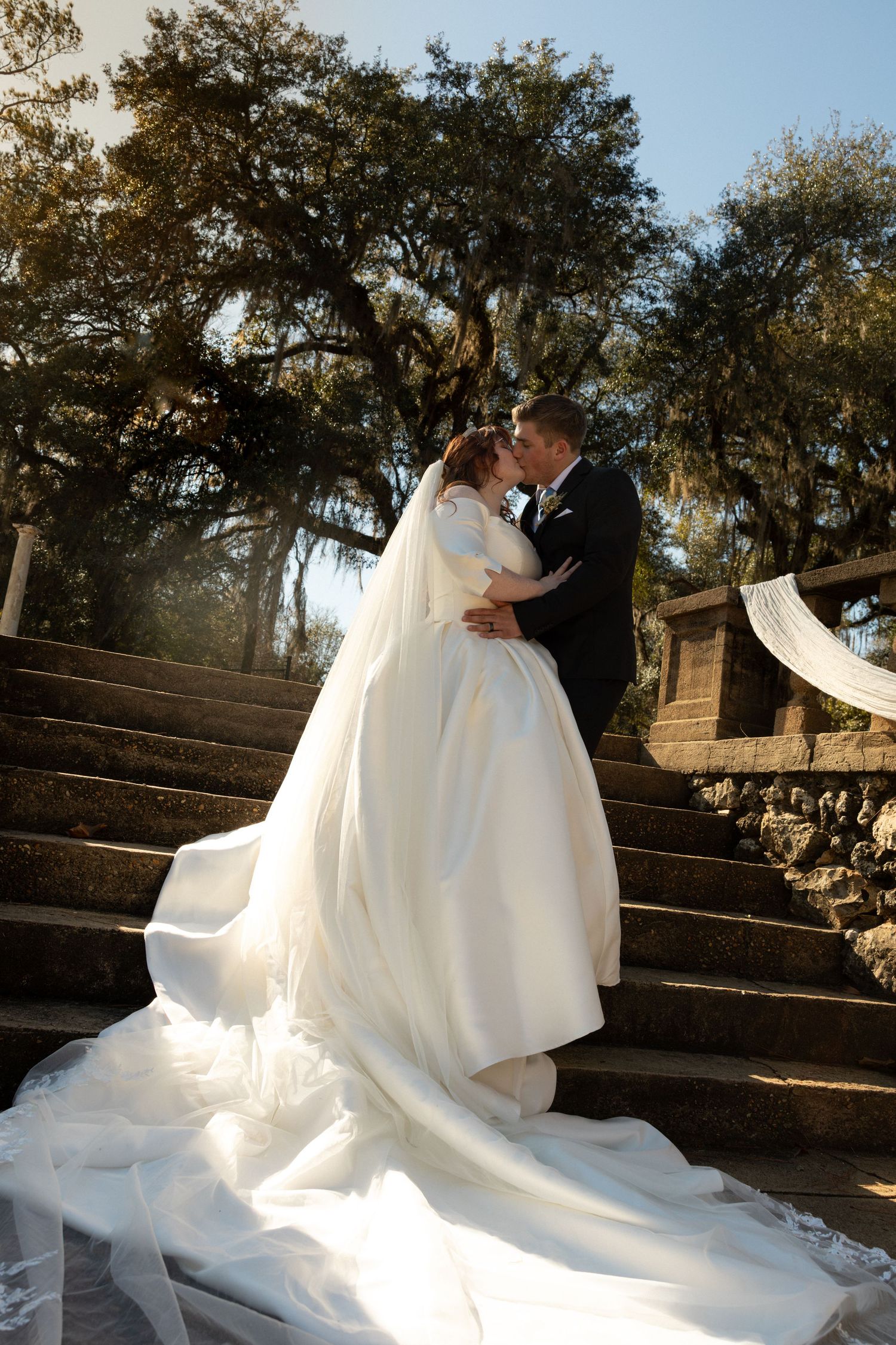 A romantic wedding couple shares an intimate moment on rustic stone steps surrounded by autumn trees.