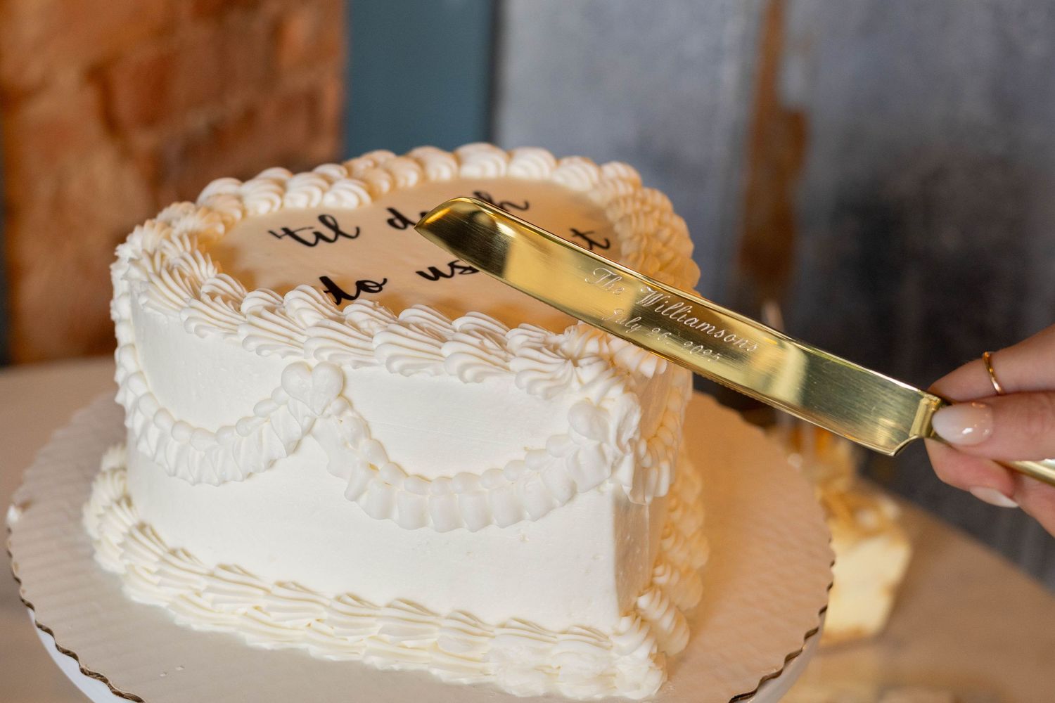 Gold cake knife cutting into a white frosted cake decorated with piped lace patterns and dots.