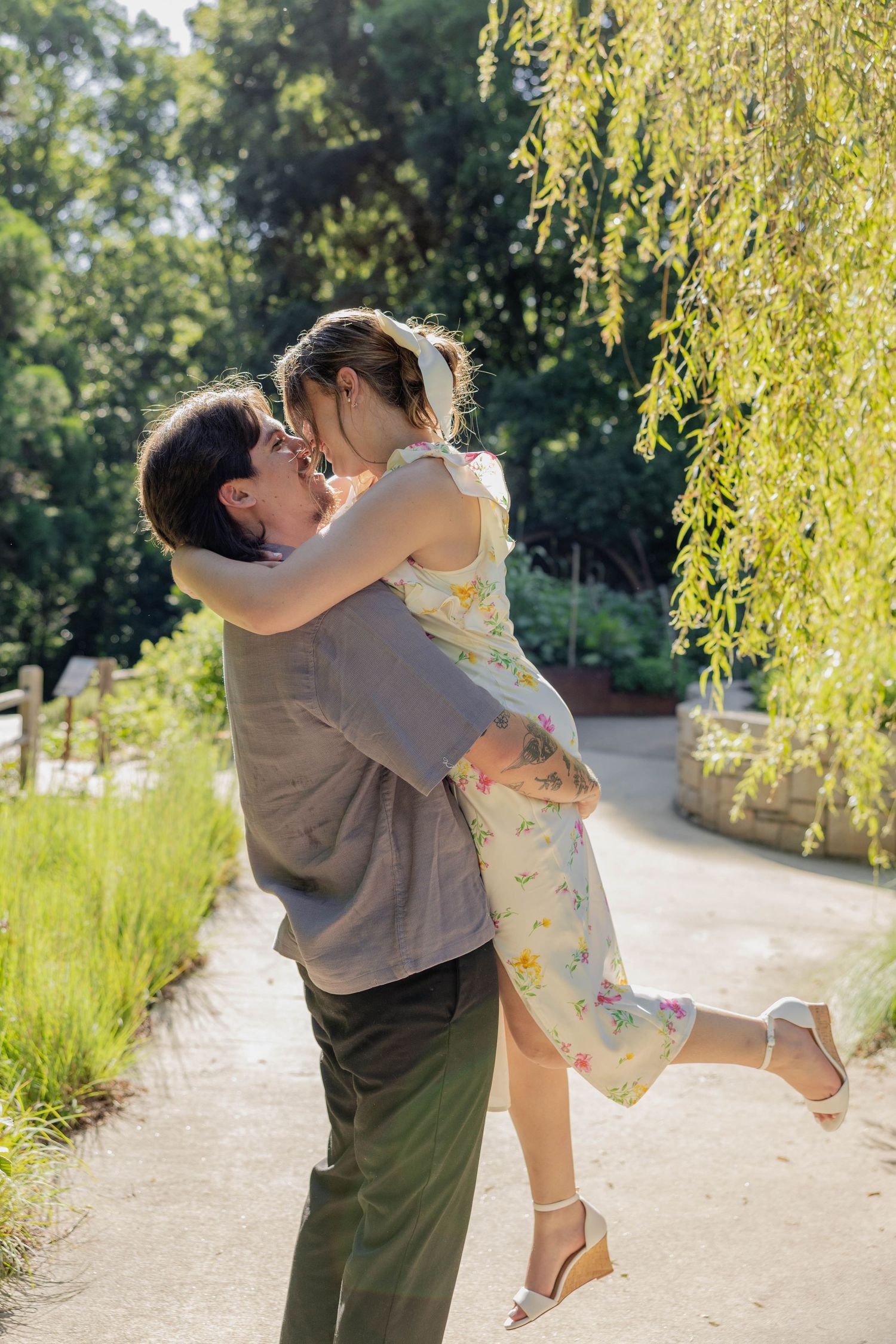 A romantic embrace on a garden path with weeping willow branches overhead on a sunny summer day.