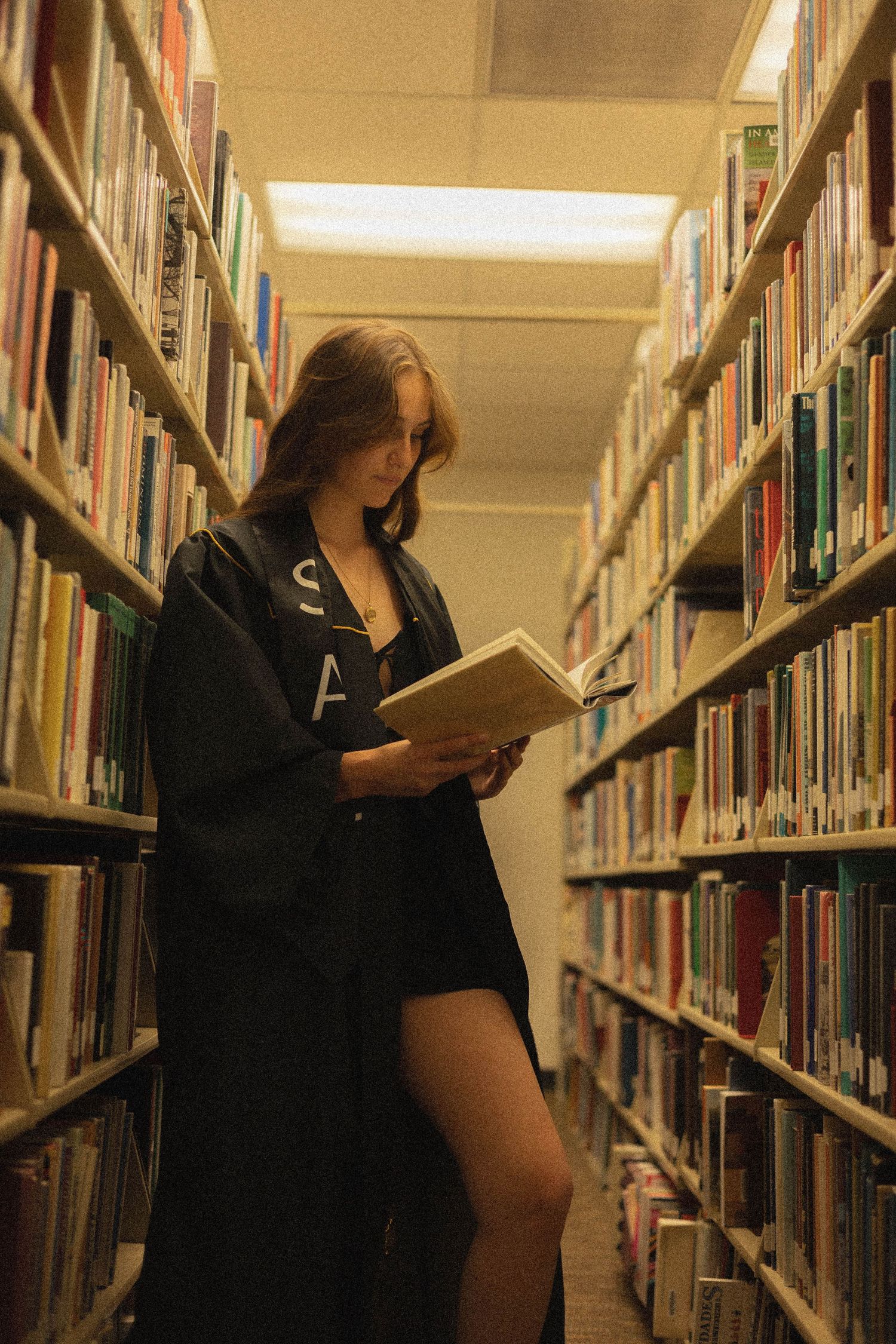Reader absorbed in a book while standing among library shelves.