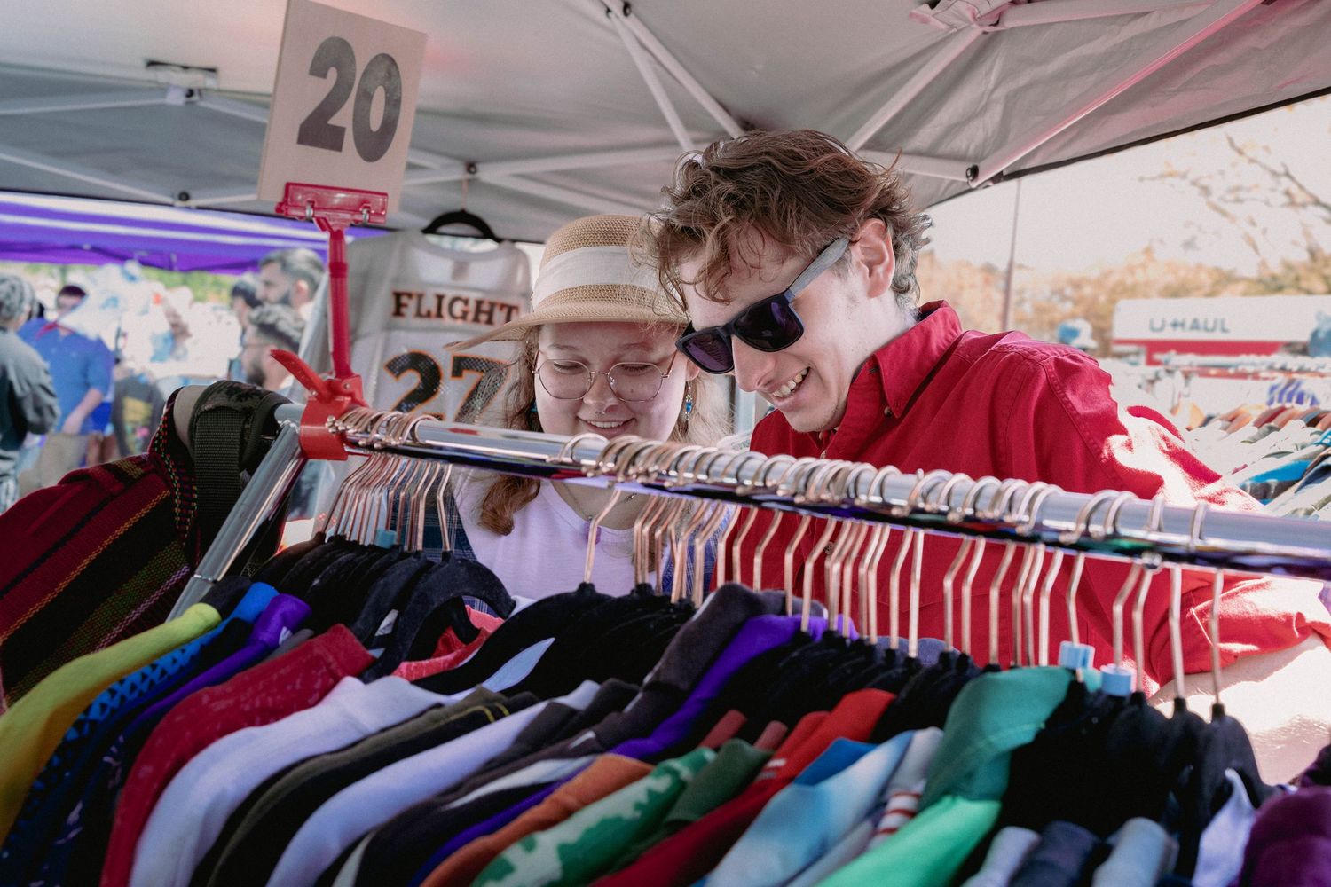 Two people look through racks of vibrant clothing at an outdoor market display.