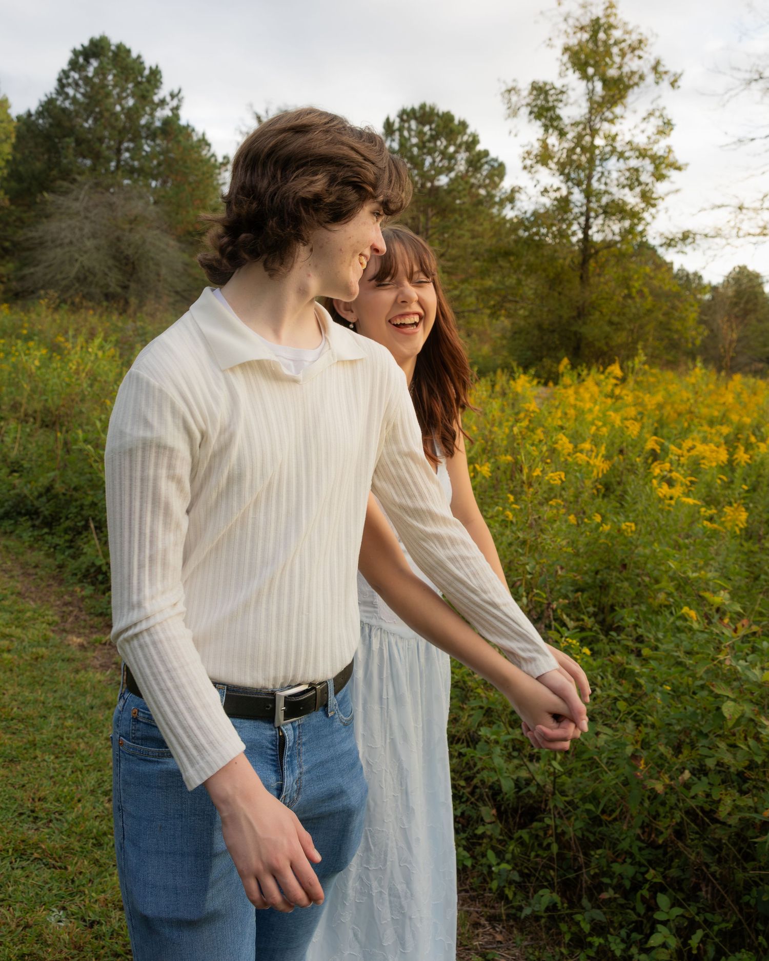 Two people share a joyful moment together while walking through a field of vibrant yellow wildflowers at sunset.