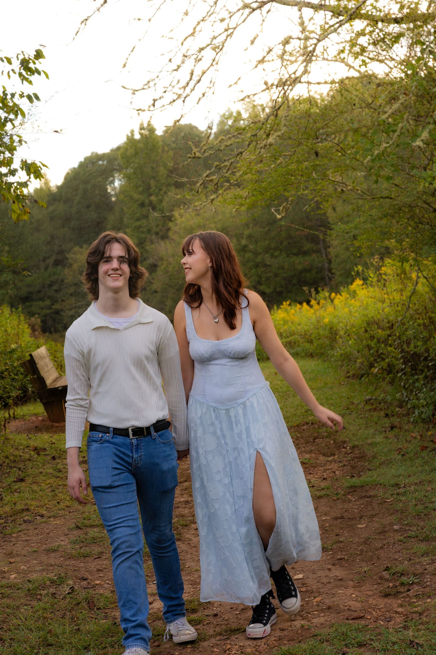 A couple walking together on a dirt path through an orchard at sunset.