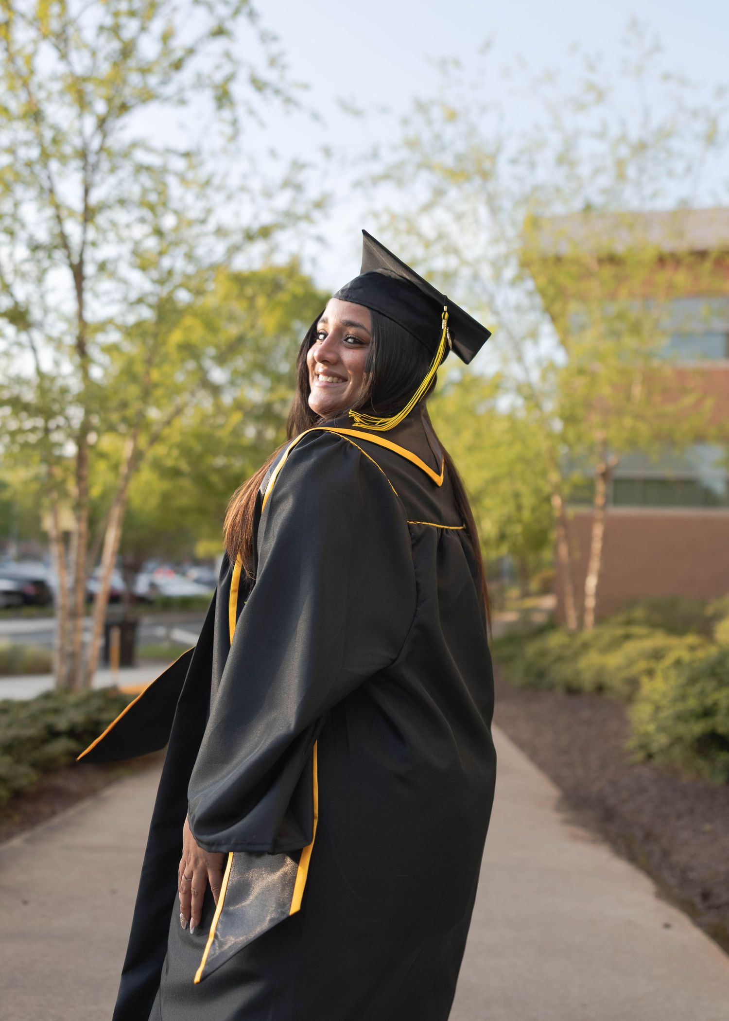 Kennesaw State University Graduate in black and gold academic regalia looking back while walking on campus path.
