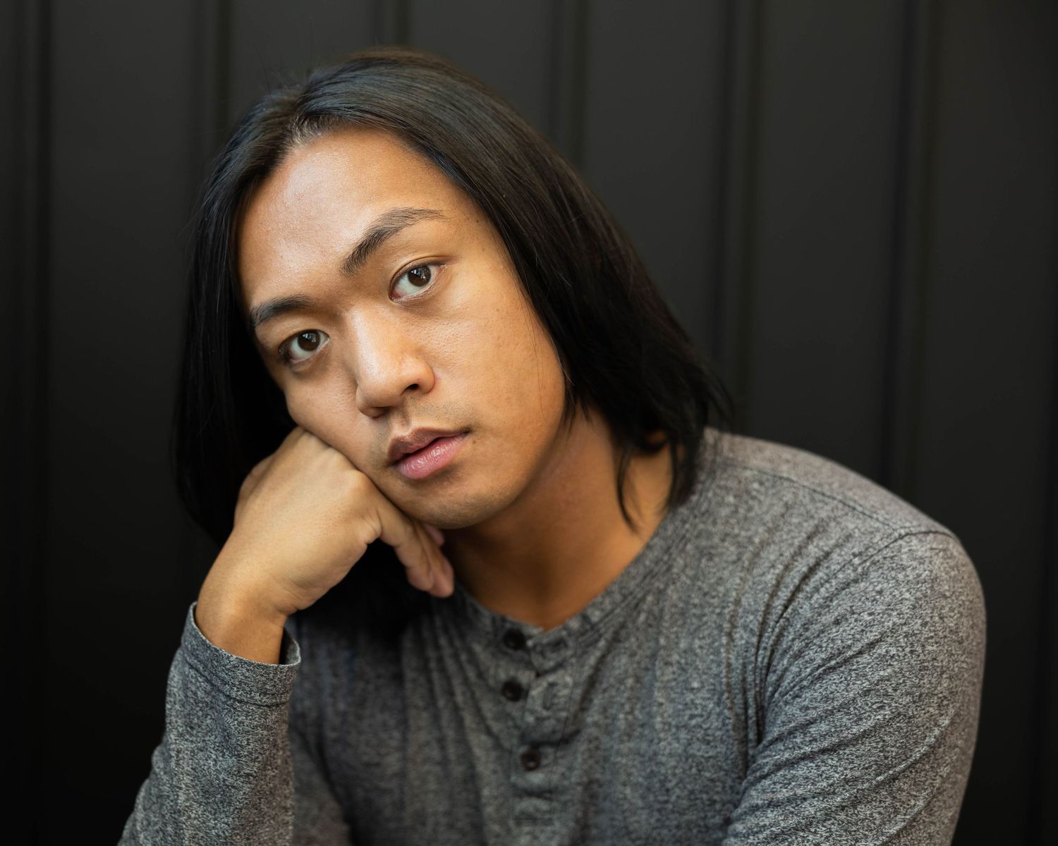 Person in gray sweater poses for expressive portrait series against dark background, showing different angles and moods.