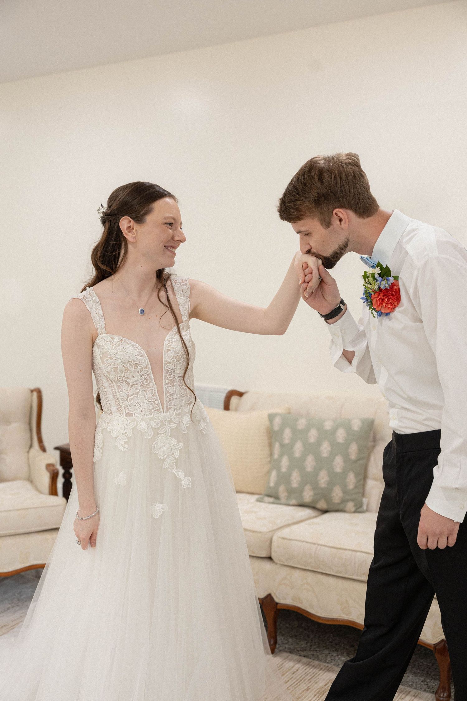 A couple shares a joyful dancing moment in a bright room with one wearing a white wedding gown.