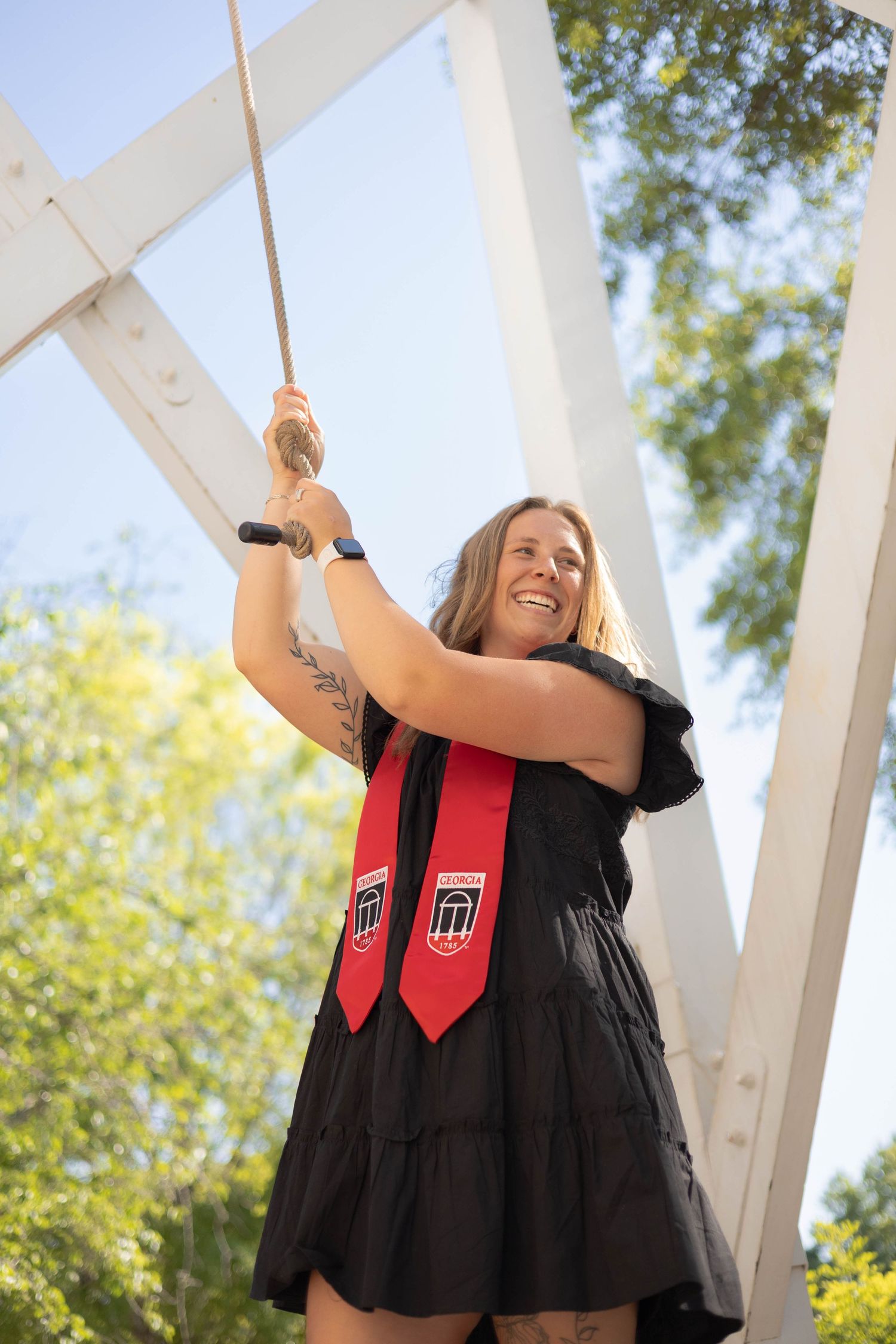 University of Georgia Graduate in black dress ringing ceremonial bell during graduation celebration.