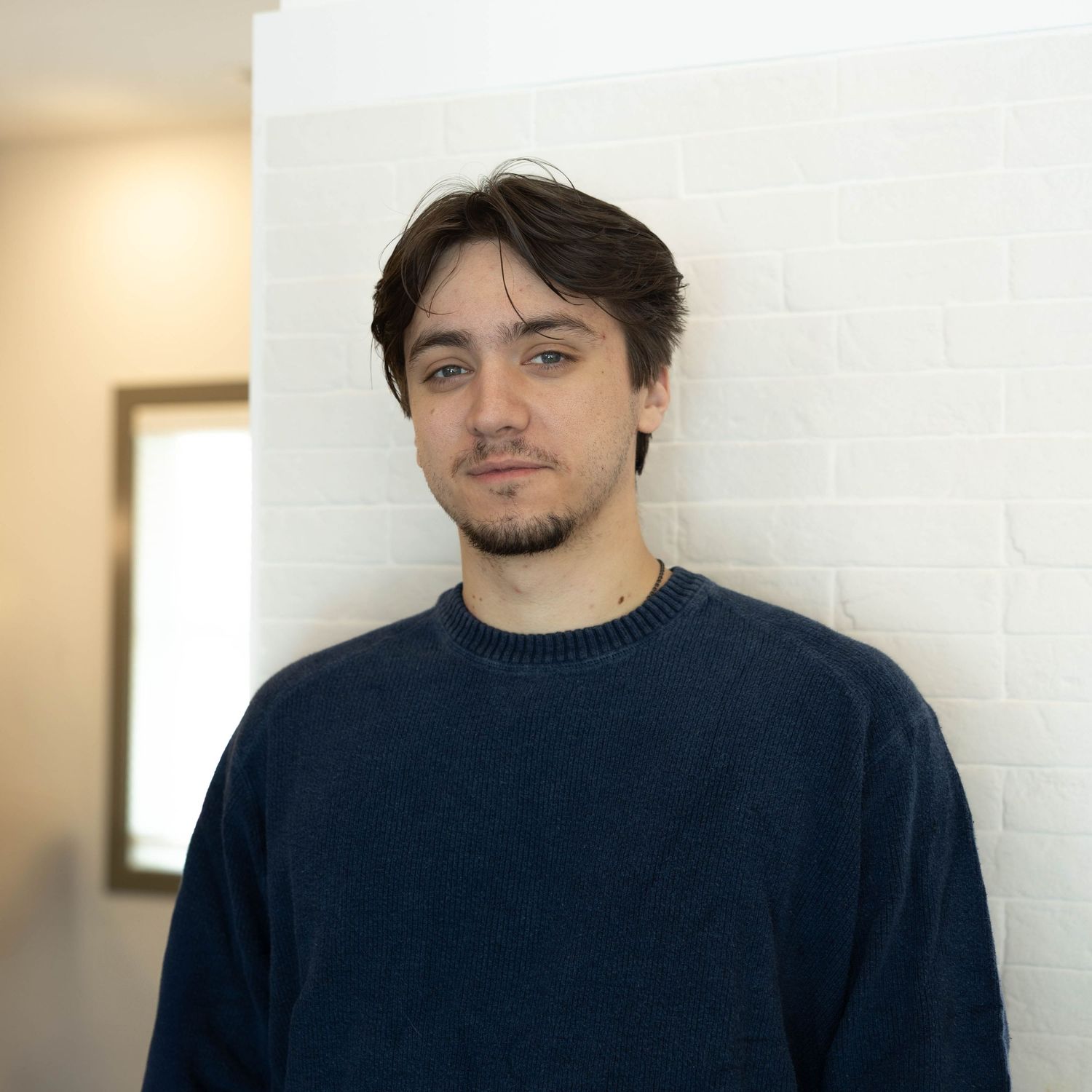 A series of headshots showing someone wearing a navy blue sweater against a light-colored wall.