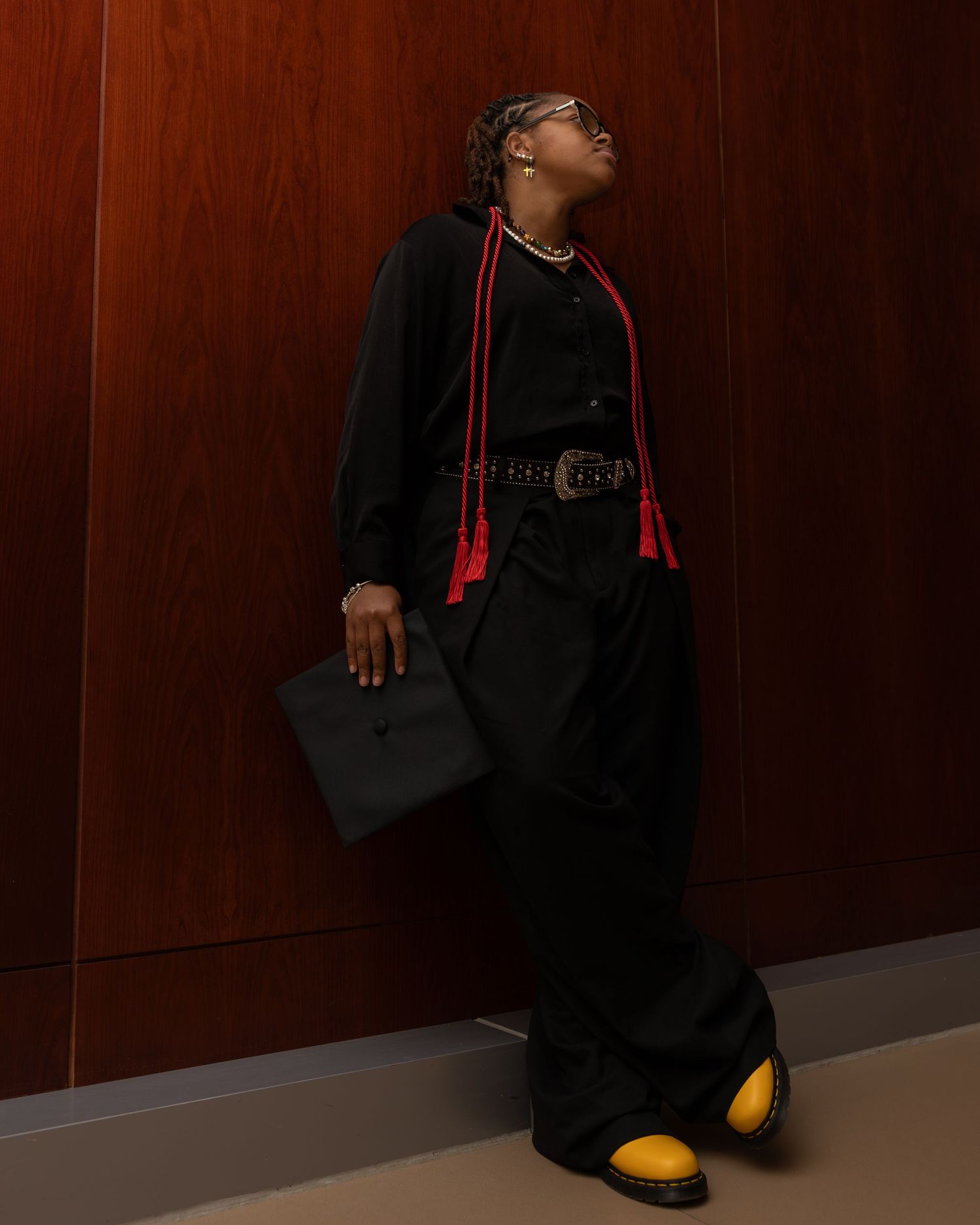 A series of photos showing someone in a black graduation gown and yellow shoes posing against a dark wood-paneled wall.