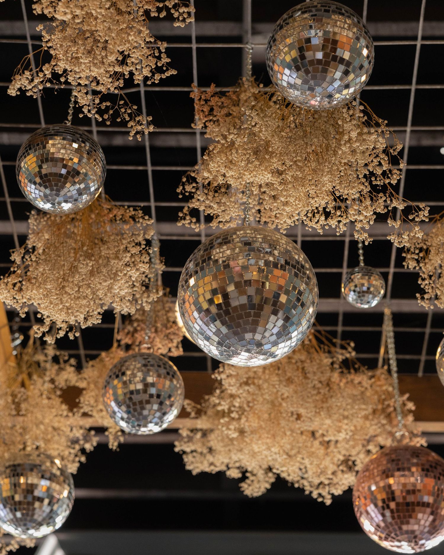 Hanging disco balls and dried baby's breath create an ethereal party decoration display against a dark ceiling.
