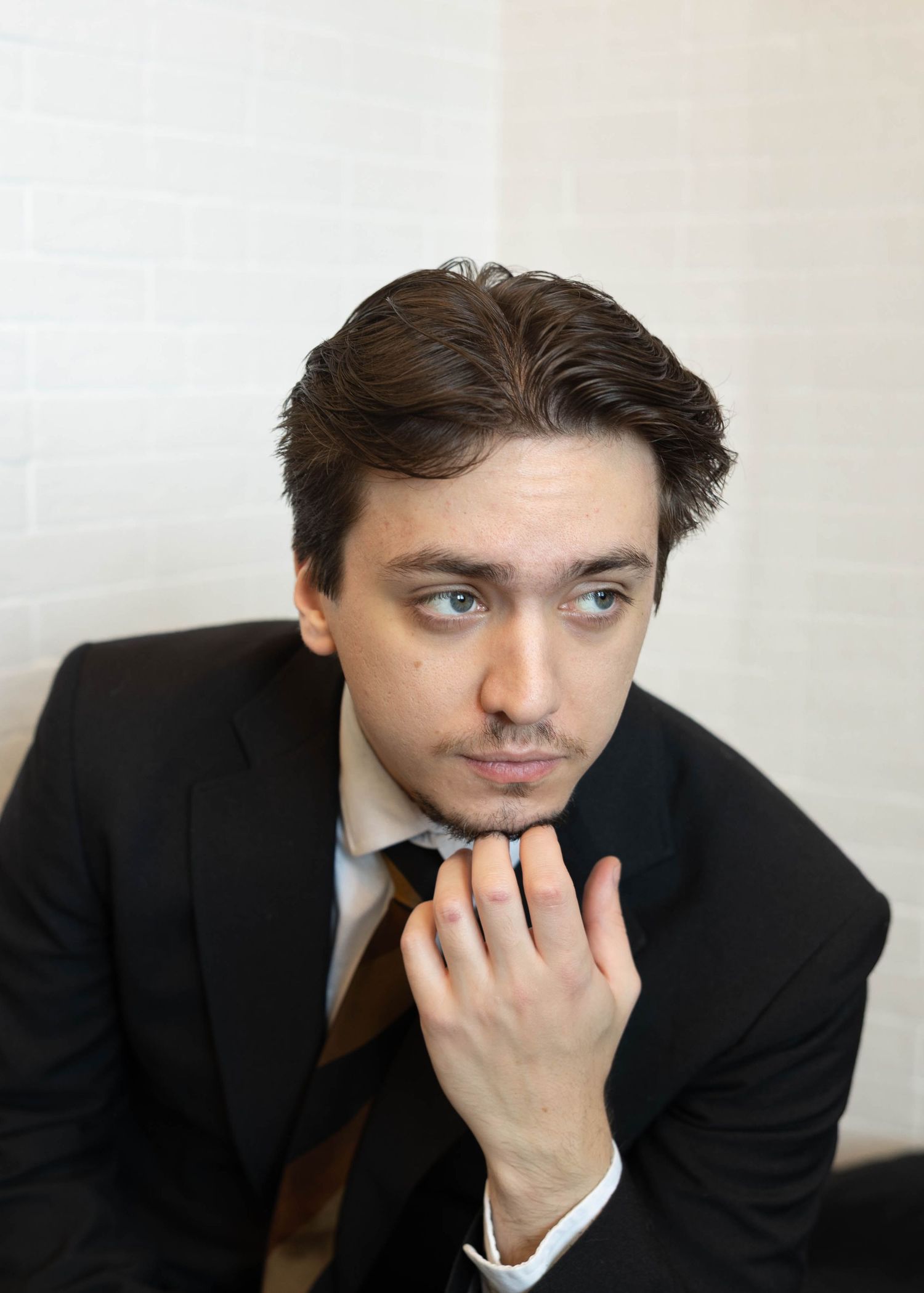 Professional headshot of someone in a black suit and tie with thoughtful pose resting hand on chin.