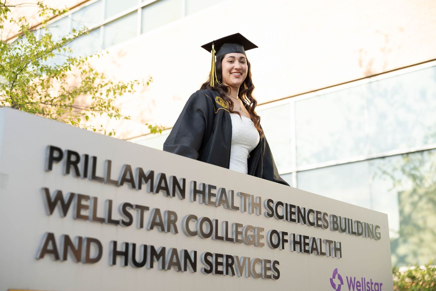 Kennesaw State University Graduate posing outside the Prillaman Health Sciences Building at Wellstar College.