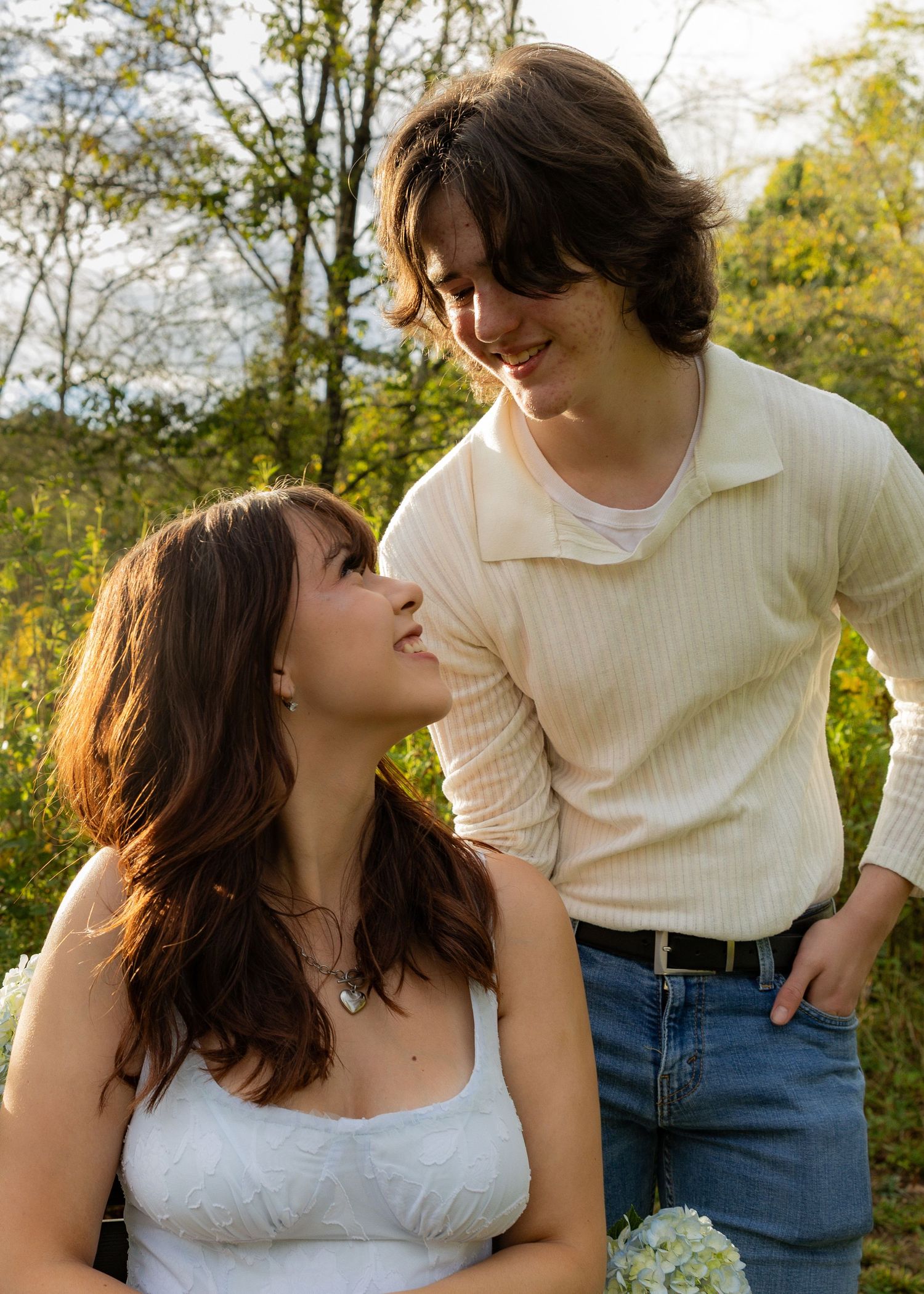 A romantic couple shares an intimate moment in a sunlit garden setting with natural greenery in the background.