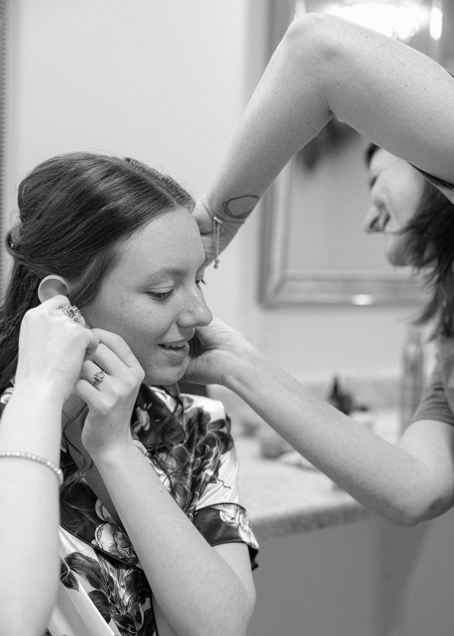 Makeup artist applies cosmetics to a client wearing a floral print top in black and white photograph.