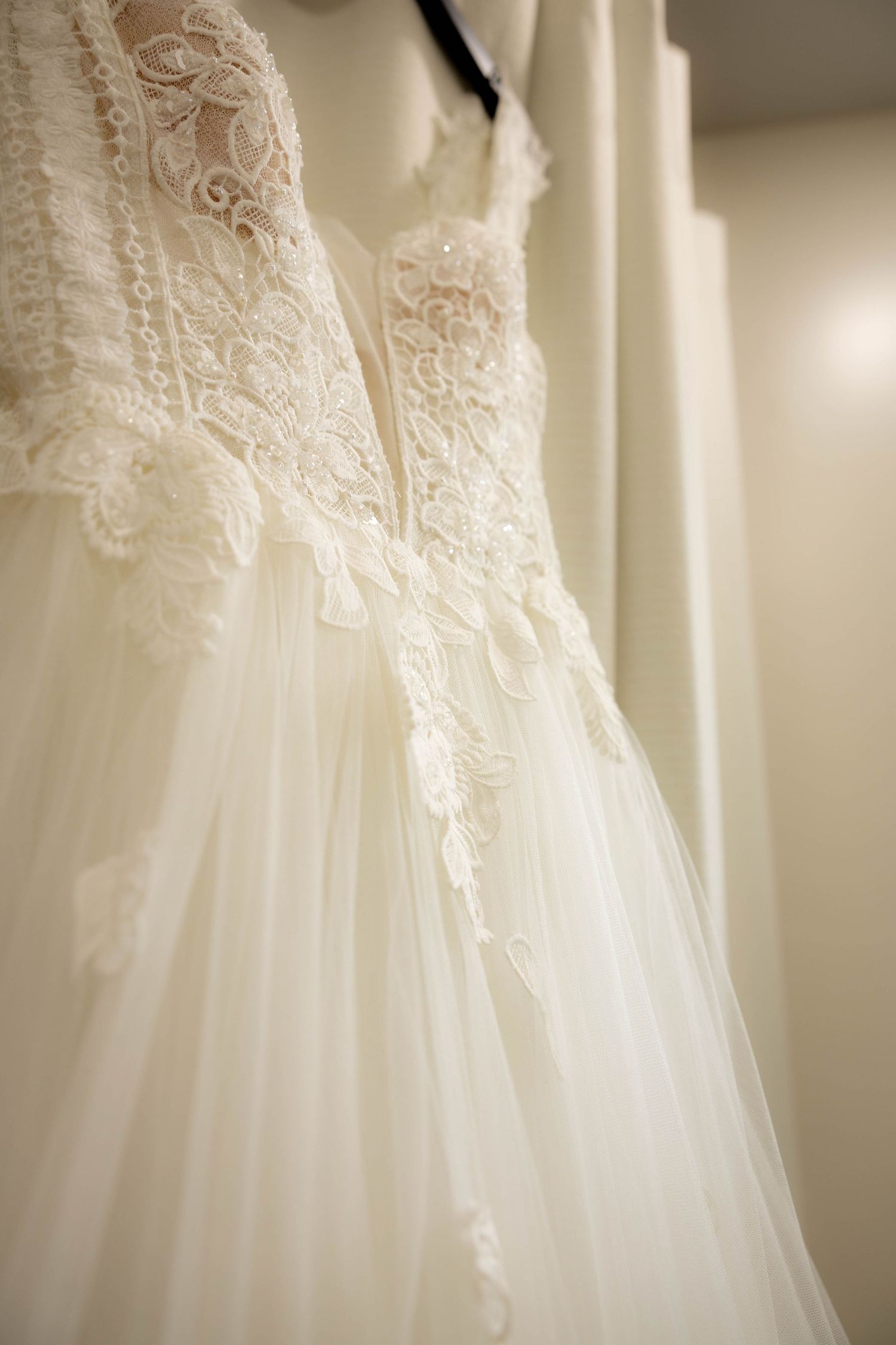 Close-up detail of an elegant white wedding dress with delicate lace embellishments and tulle skirt hanging on display.