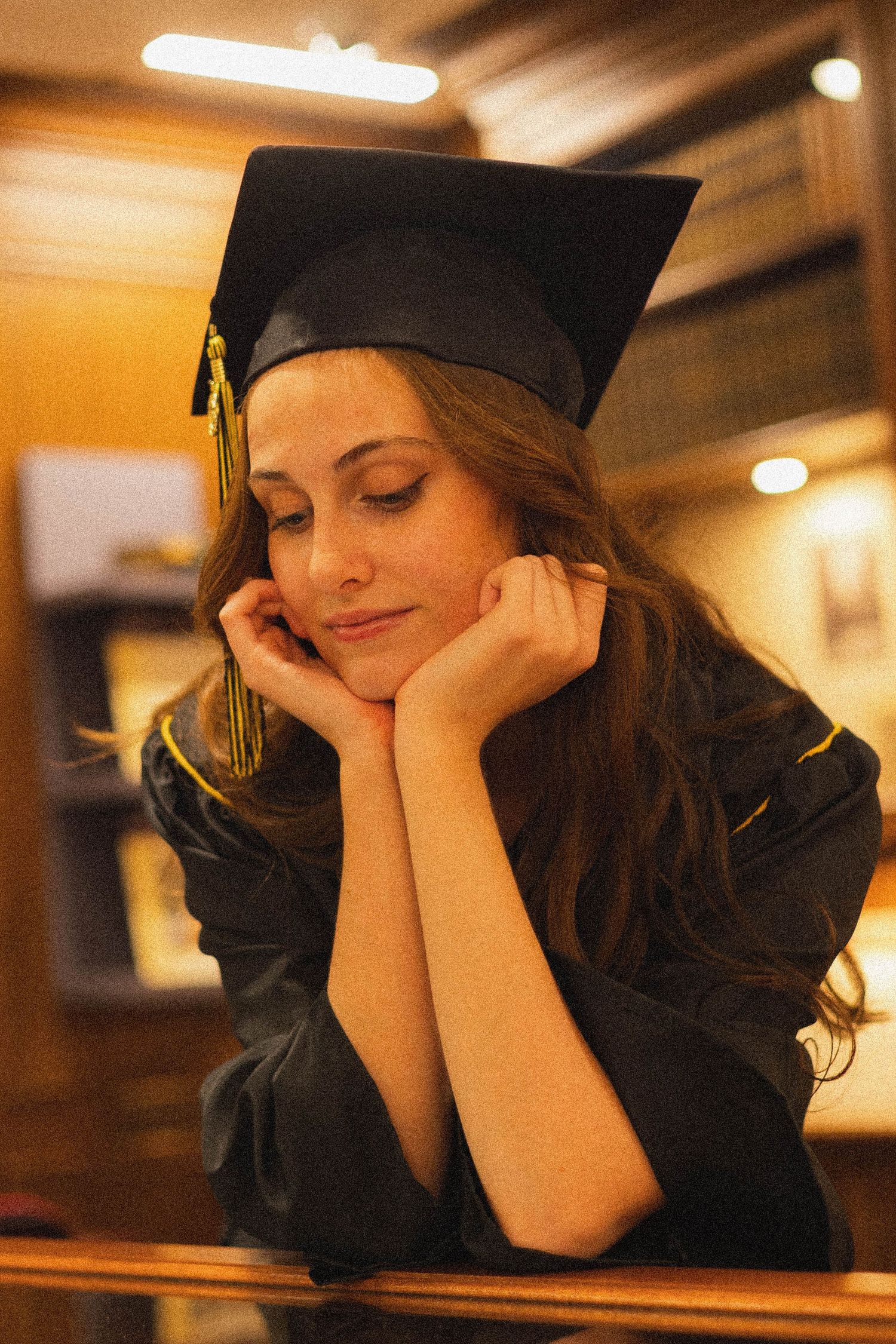 Graduate in traditional cap and gown poses thoughtfully.