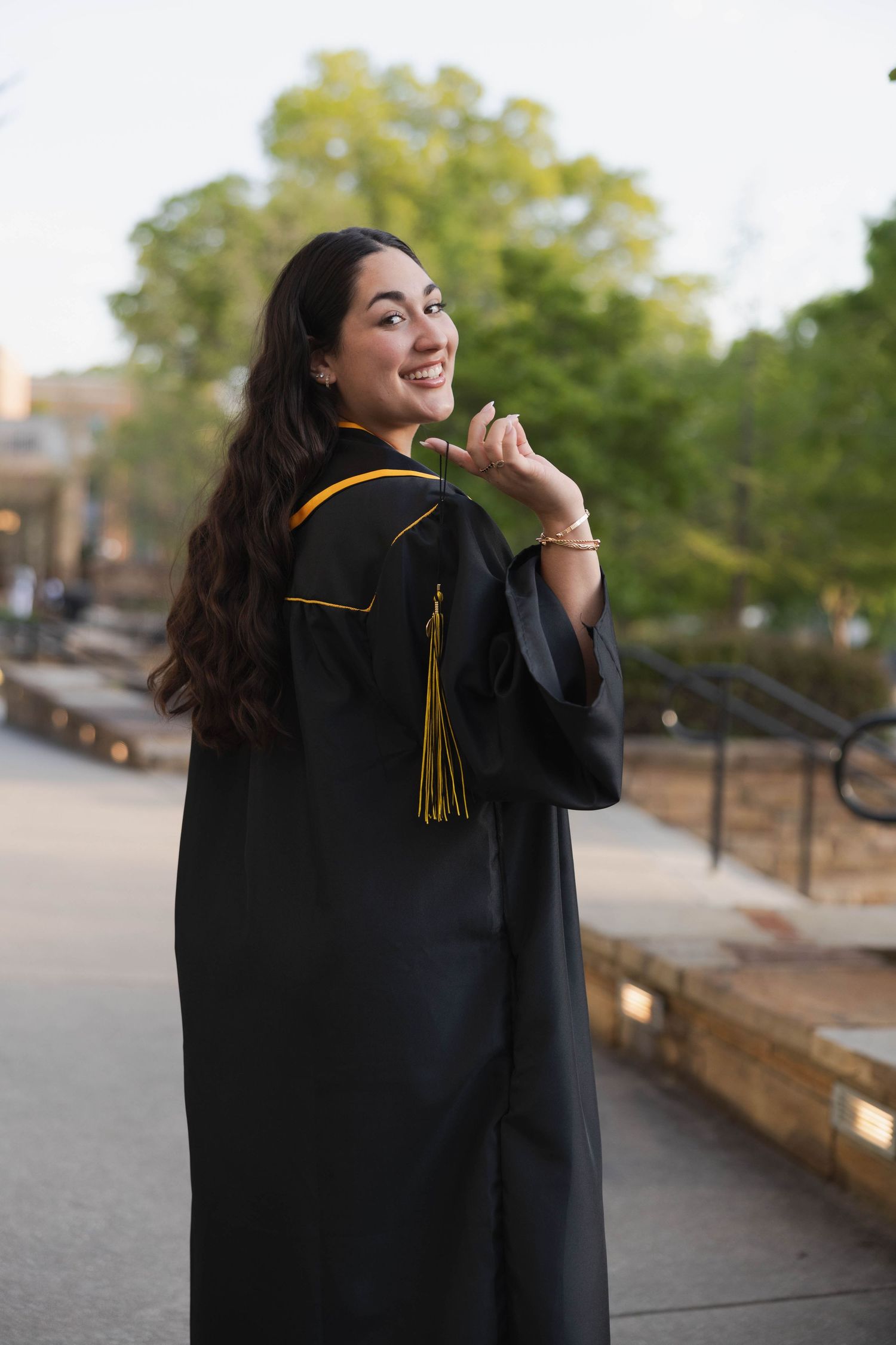 Kennesaw State University Graduate in black academic regalia with gold tassel posing outdoors on campus.