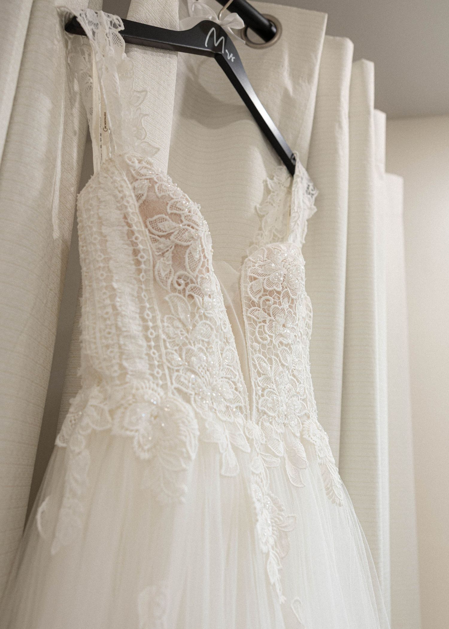 White wedding dresses hanging on display racks in a bridal boutique showing delicate lace details and various silhouettes.