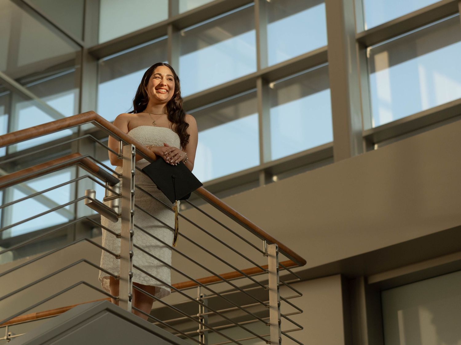 Kennesaw State University Graduate in cap and gown posing on modern indoor balcony with metal railings.