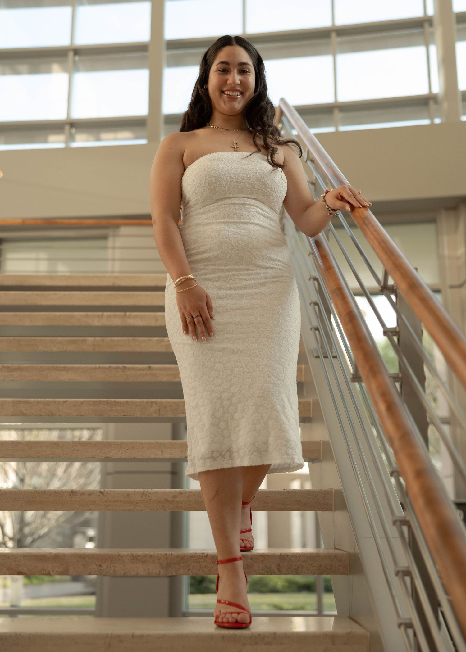 Person in white dress poses gracefully on modern staircase with metal railings in bright interior setting.