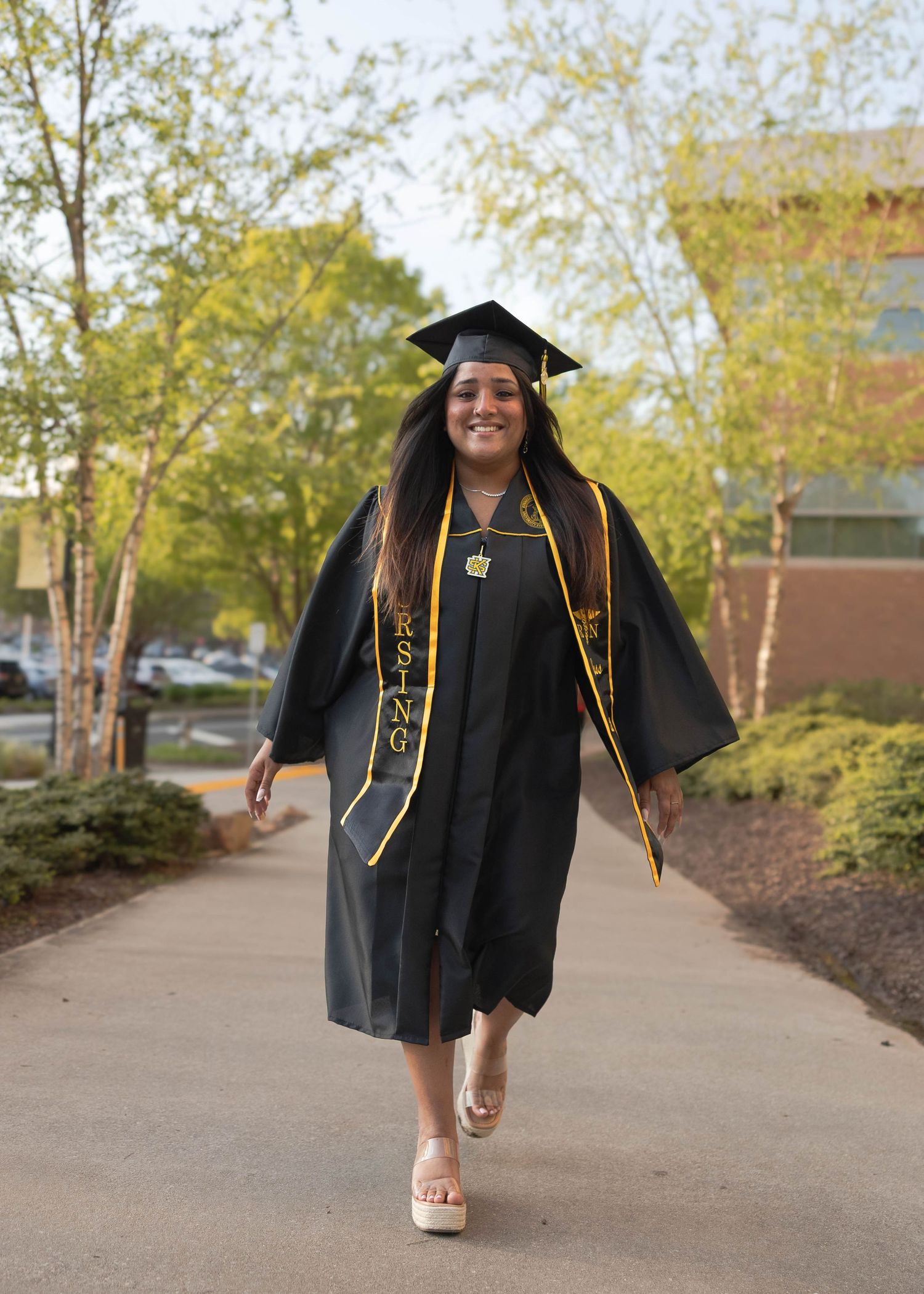 Kennesaw State University Graduate in academic regalia walking on campus sidewalk during autumn.