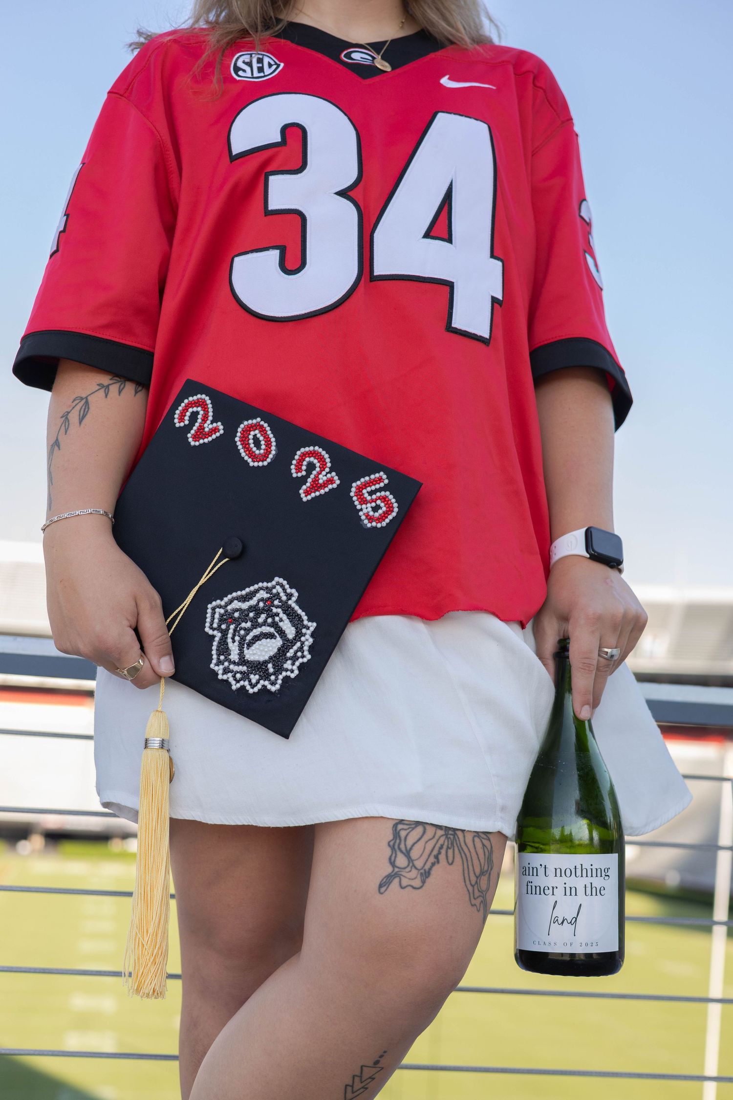 A person wearing a University of Georgia red #34 jersey holding a graduation cap and bottle while celebrating.