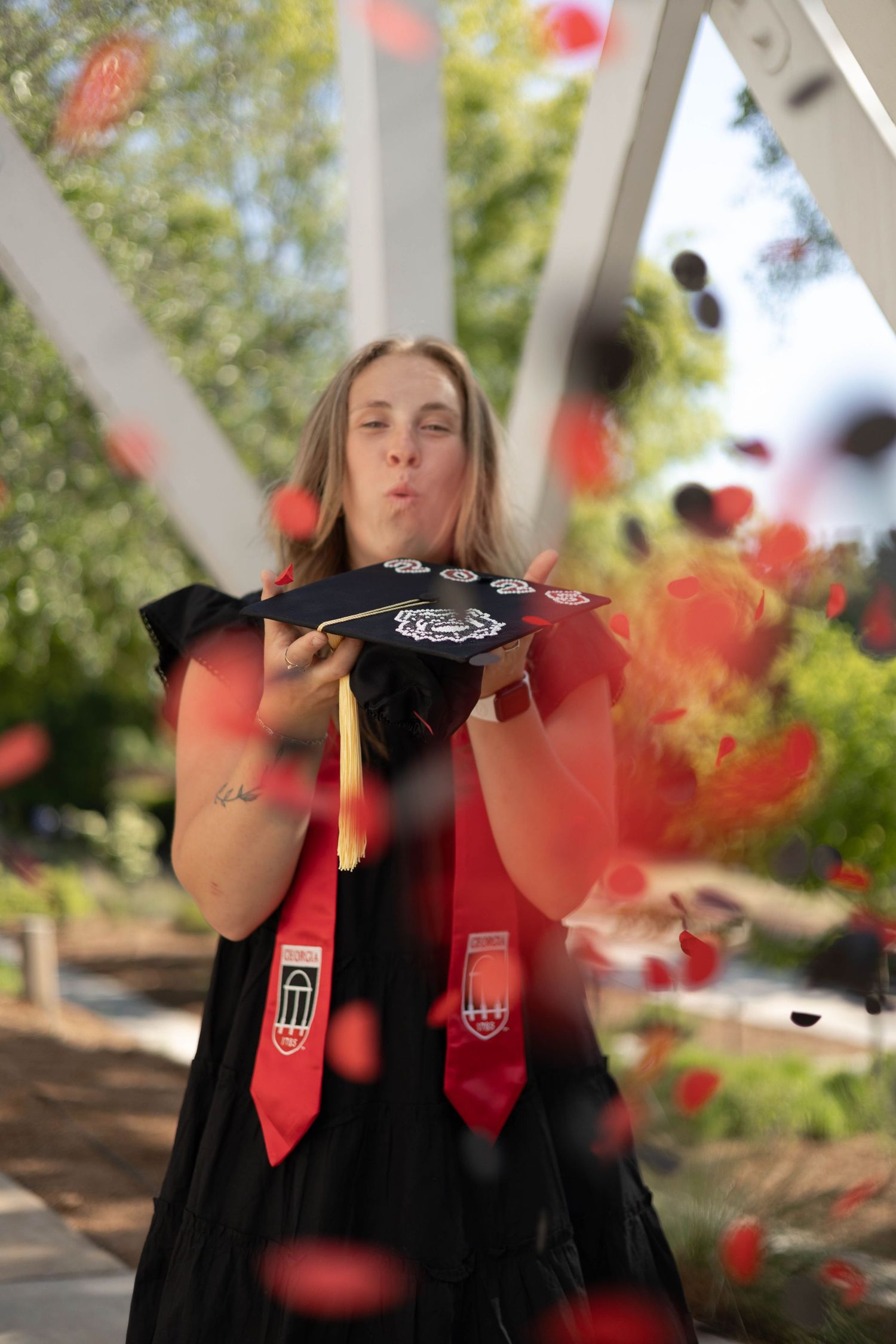 University of Georgia Graduate in black dress celebrating with confetti and academic stoles outdoors.