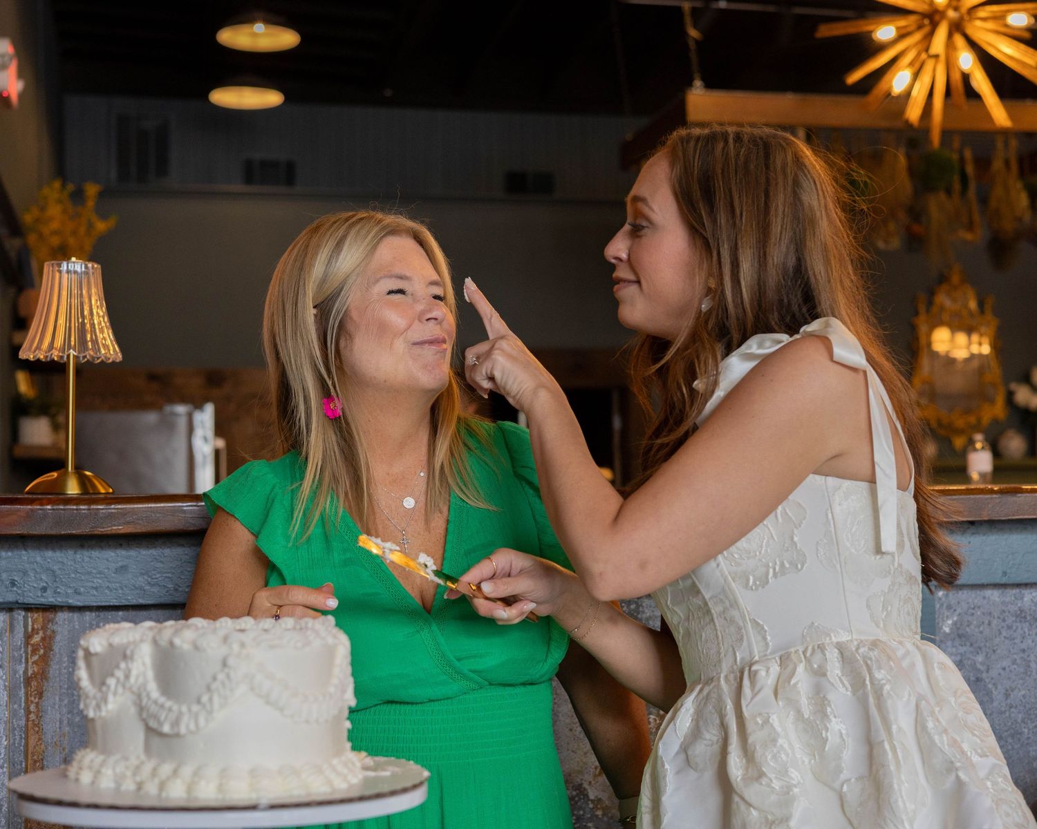 People celebrating at an indoor party with decorative lights and a white cake in an elegant venue setting.