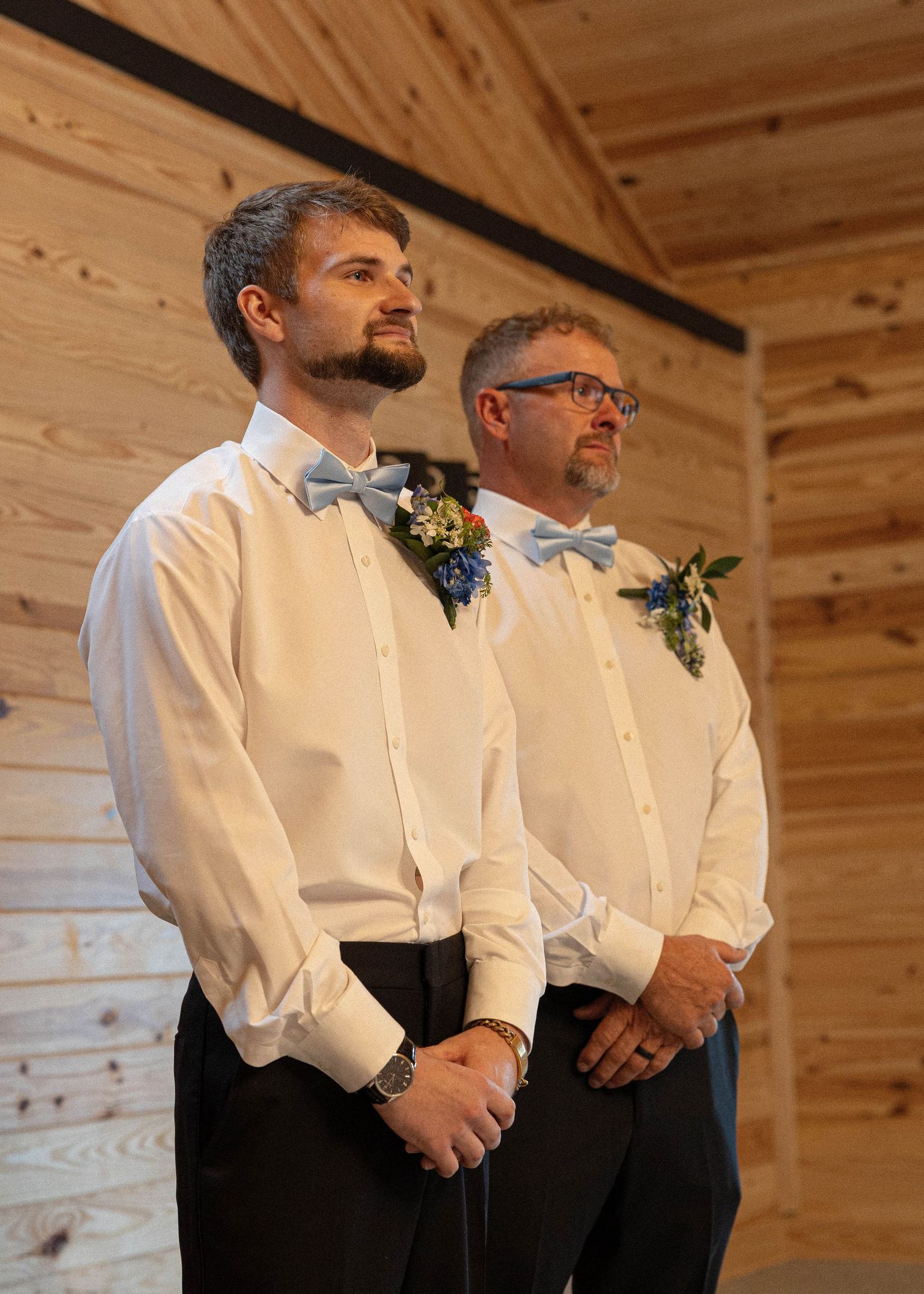 Groomsmen in white shirts and bow ties stand in a row at a rustic wooden venue.