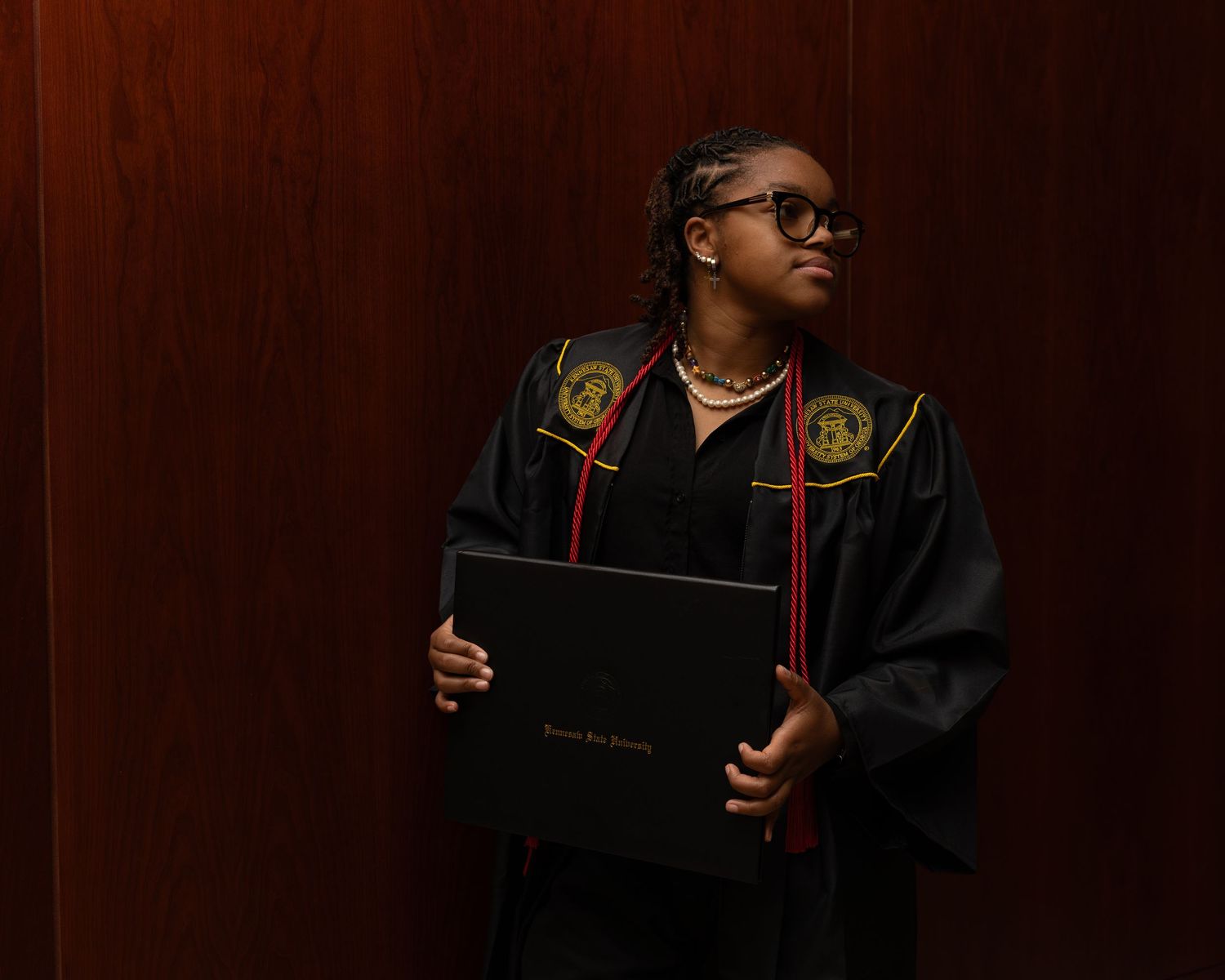 A series of eight dark, moody graduation portraits showing a person in academic regalia against a brown background.