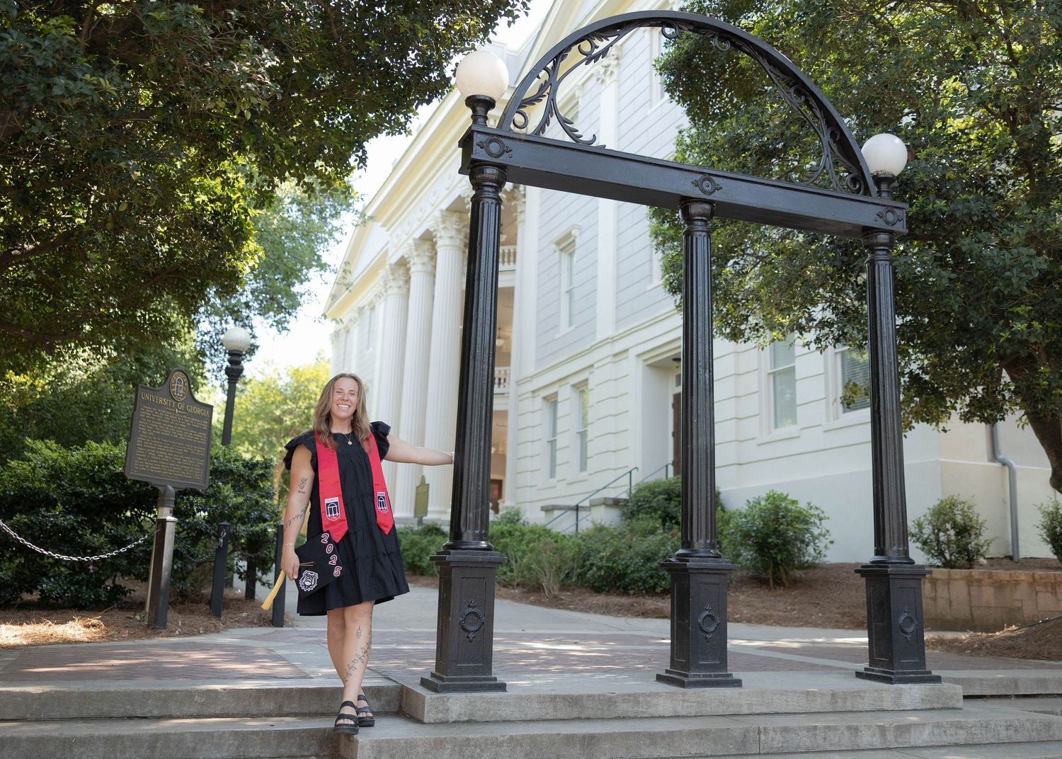 University of Georgia Student wearing a dress poses under iconic archway on college campus.