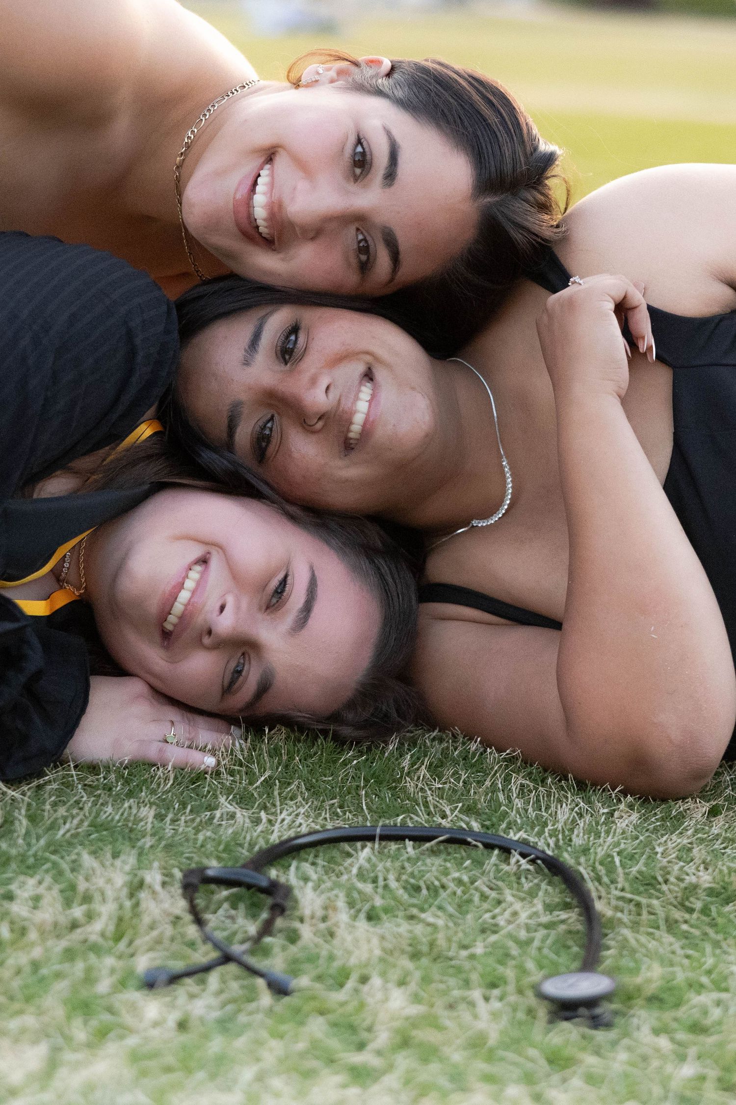 Three graduates lying on grass taking celebratory photo together.