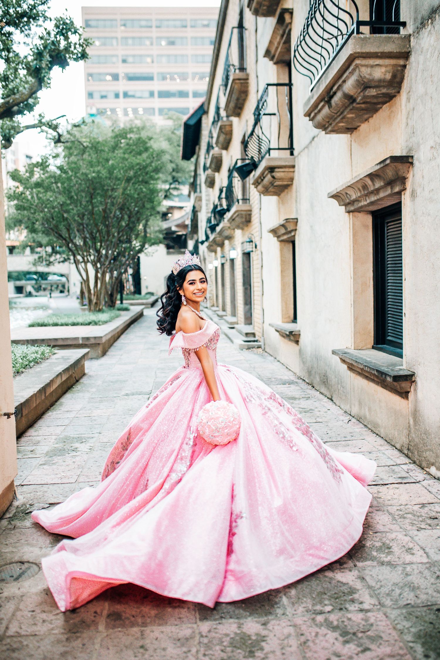Young woman in a flowing pink ball gown and tiara poses outdoors for a quinceañera photo shoot. quinceañera