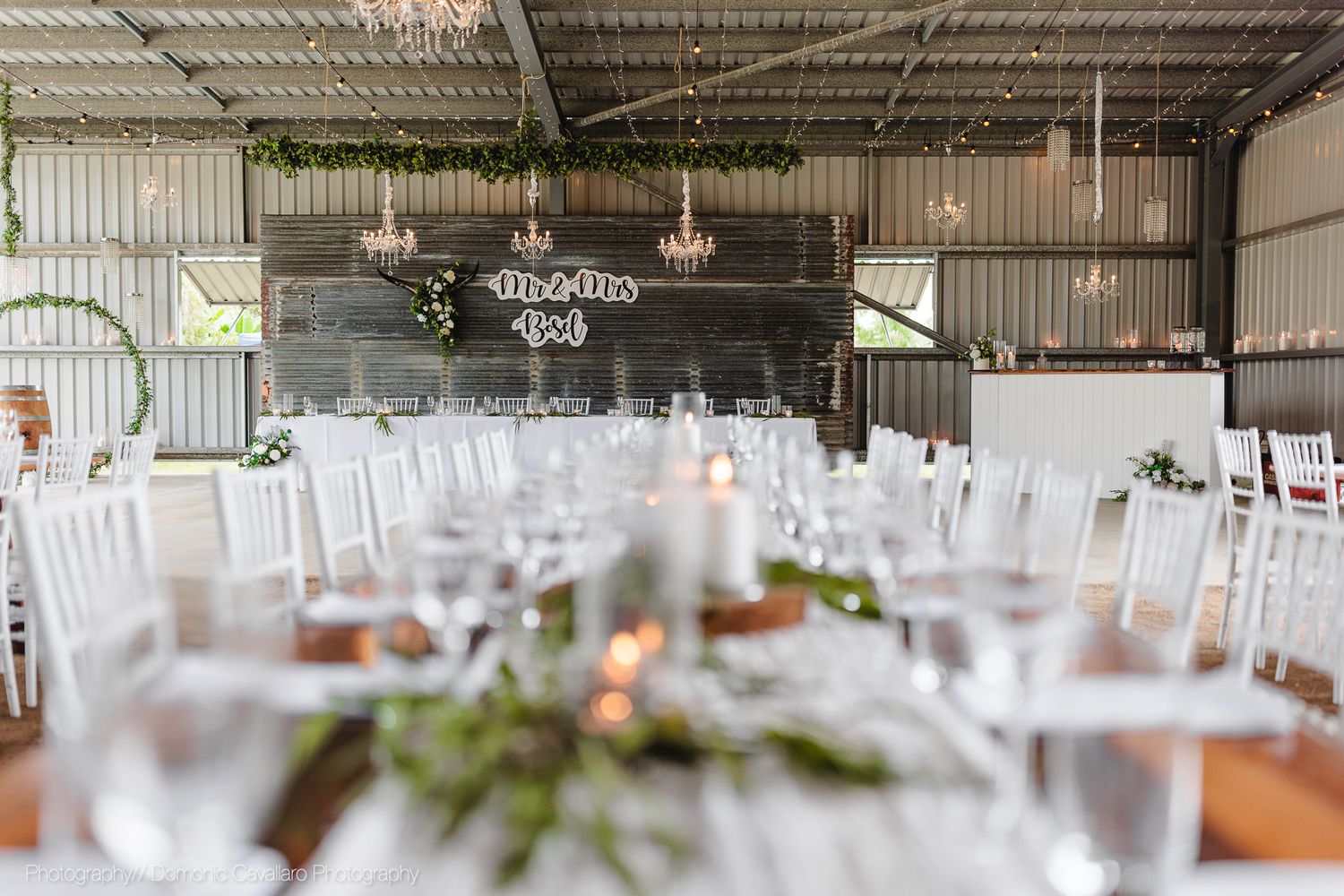 An elegant wedding reception venue setup with white chairs and floral centerpieces in a rustic indoor space.