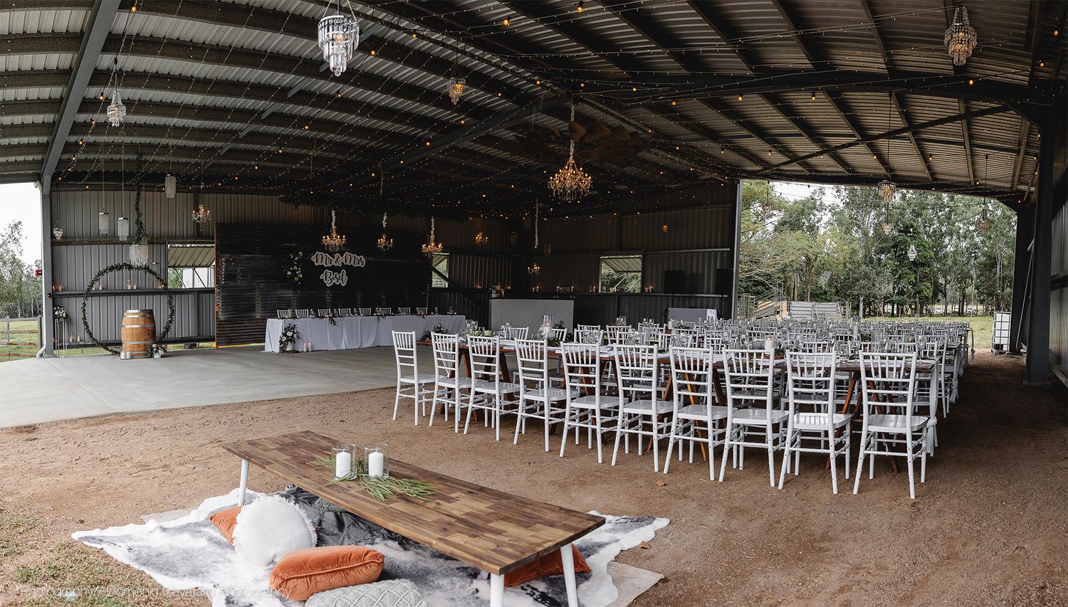 Rustic barn wedding venue with rows of white chairs and vintage pendant lights hanging from exposed beams.
