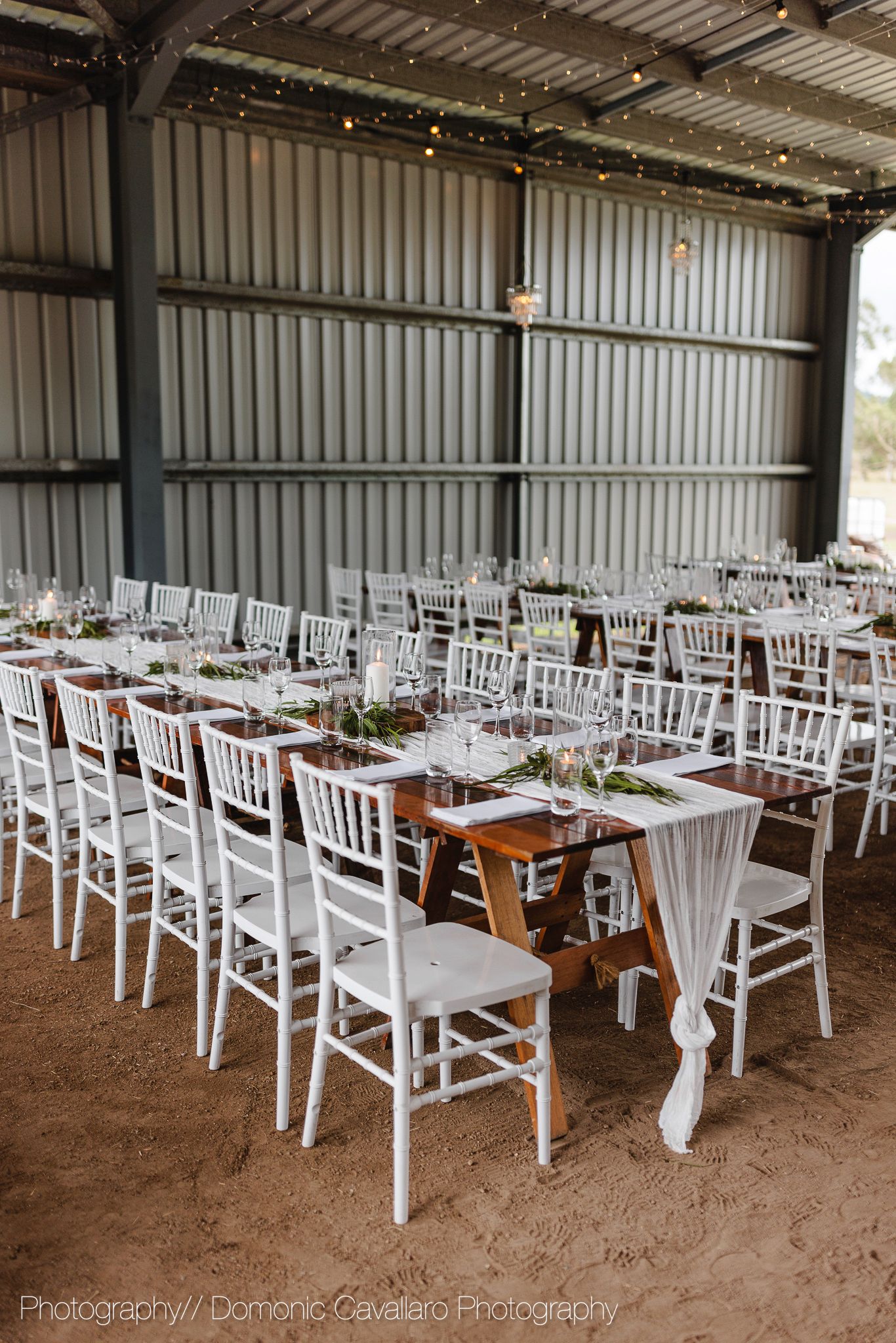 White chiavari chairs and wooden tables arranged in neat rows within an industrial event space.