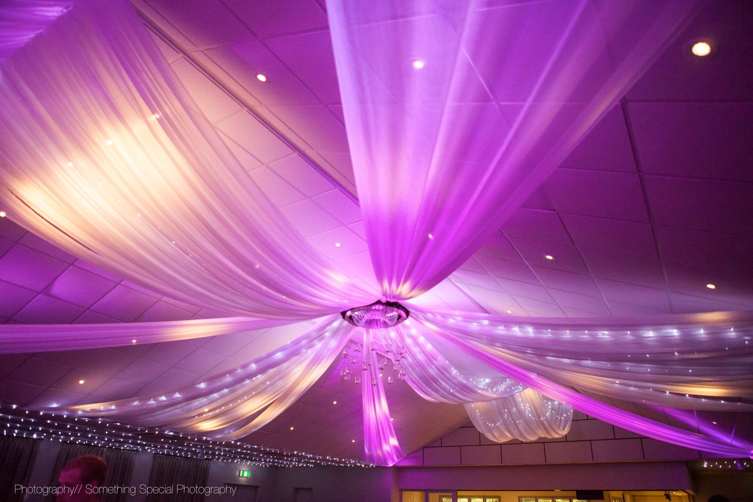 Purple and white fabric drapes elegantly from the ceiling with string lights creating a magical reception ambiance.