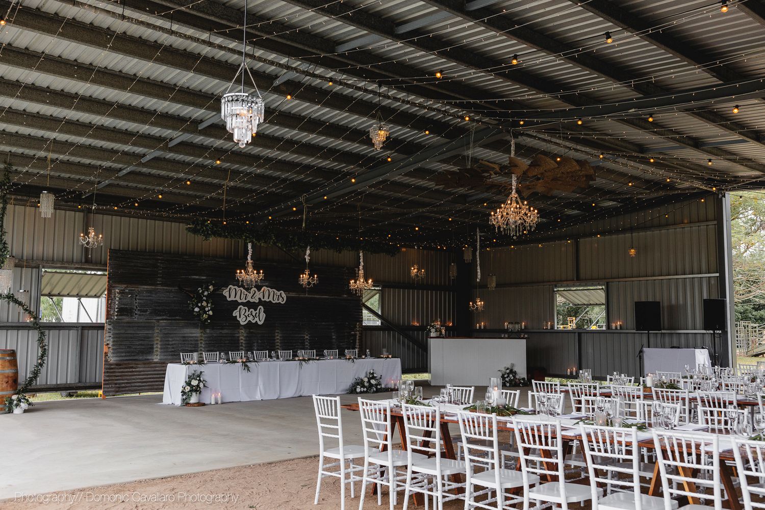 Industrial style wedding venue interior with chandeliers and white dining setup.