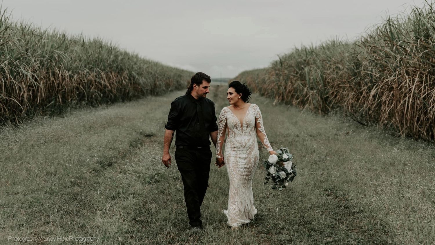 Couple walking together through a path lined with tall sugarcane fields.