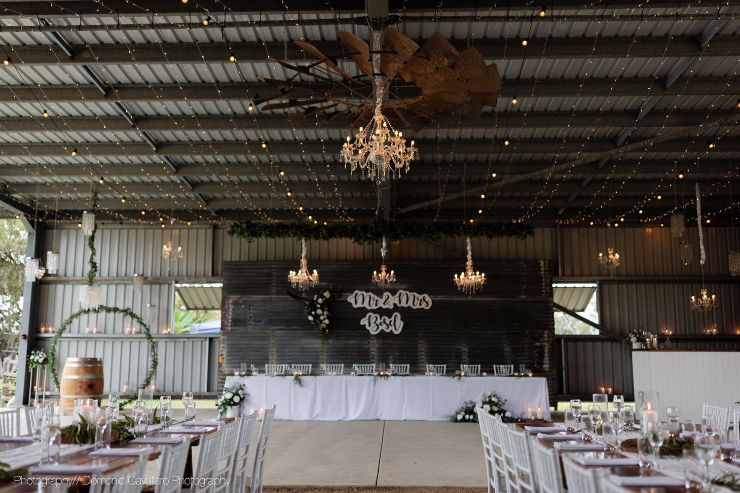 Industrial chic wedding reception space with hanging chandeliers, string lights and white table settings.